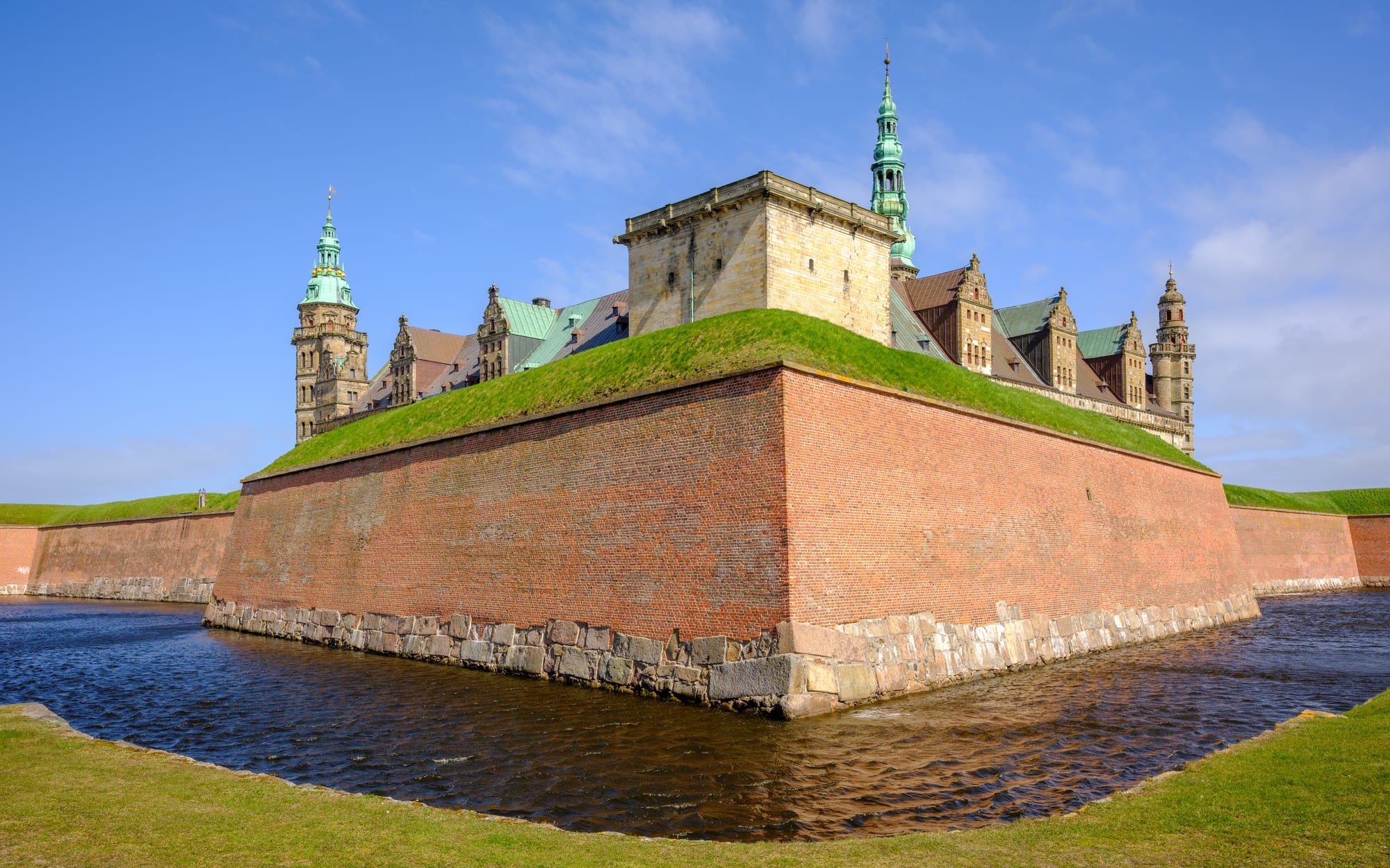 A large Renaissance castle with sandstone corners and green copper roofs, ringed by ramparts and water