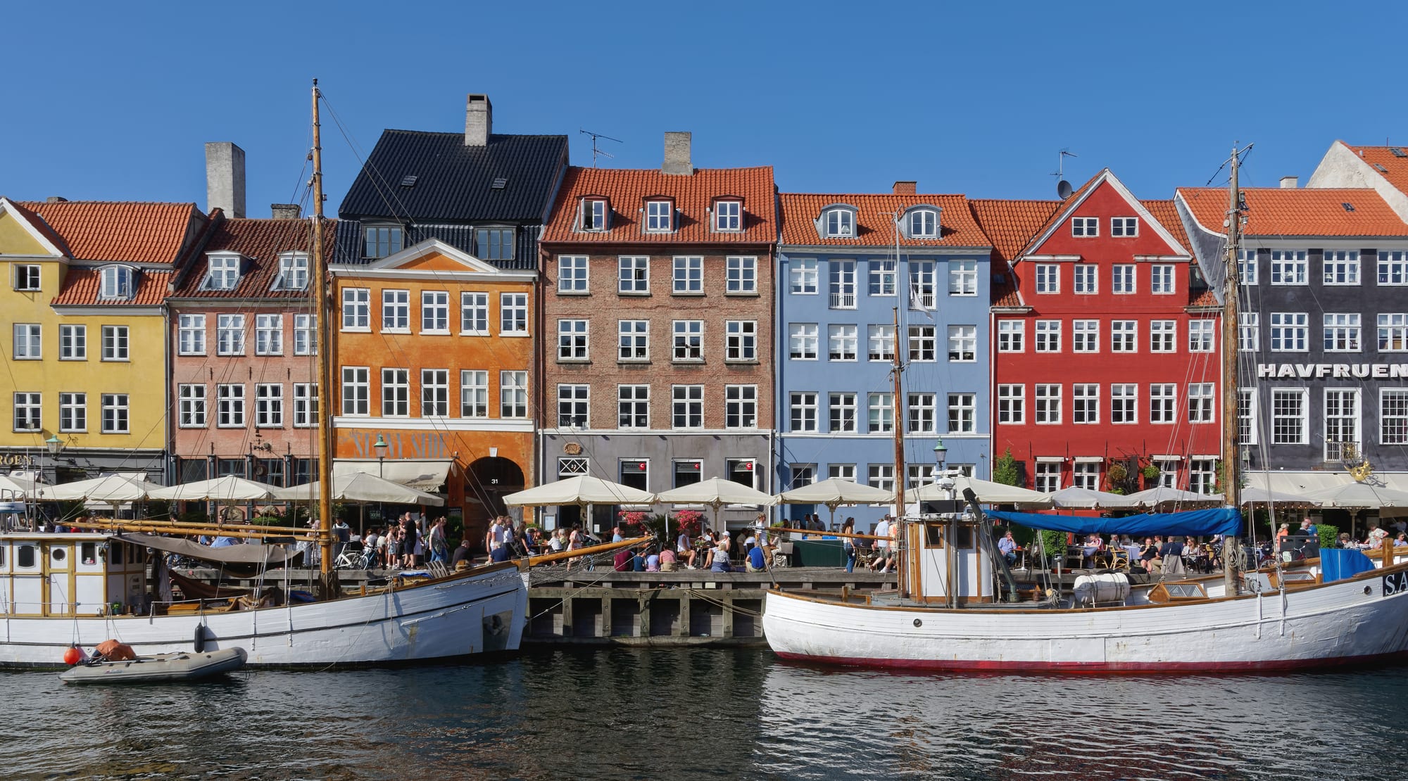 A canal lined with tall narrow townhouses painted in bright colours, wooden sailing boats moored in front