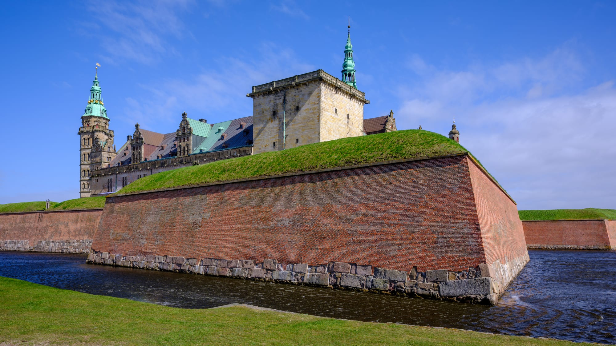 A grand Renaissance castle with green copper spires and sandstone walls behind a wide moat