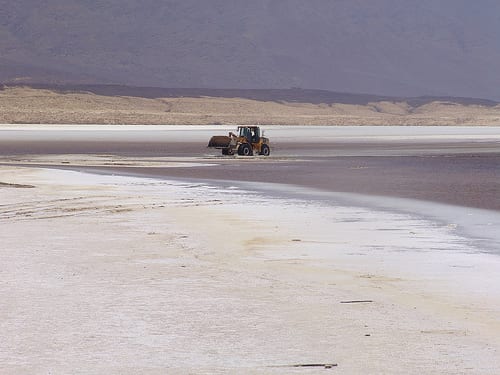 A salt flat of dazzling white crystals meeting a still turquoise lake under bare hills