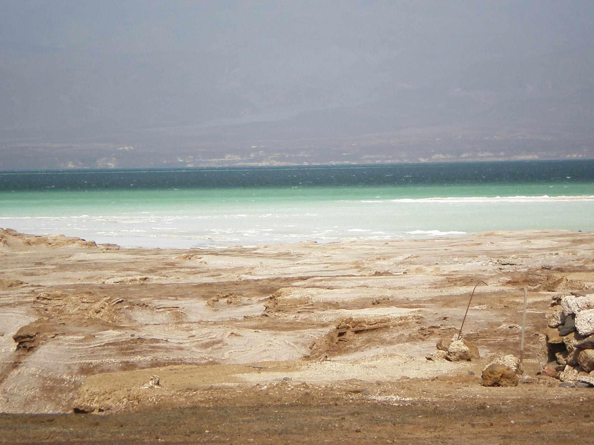 A blindingly white salt shore fringing a deep blue lake, dark volcanic hills beyond