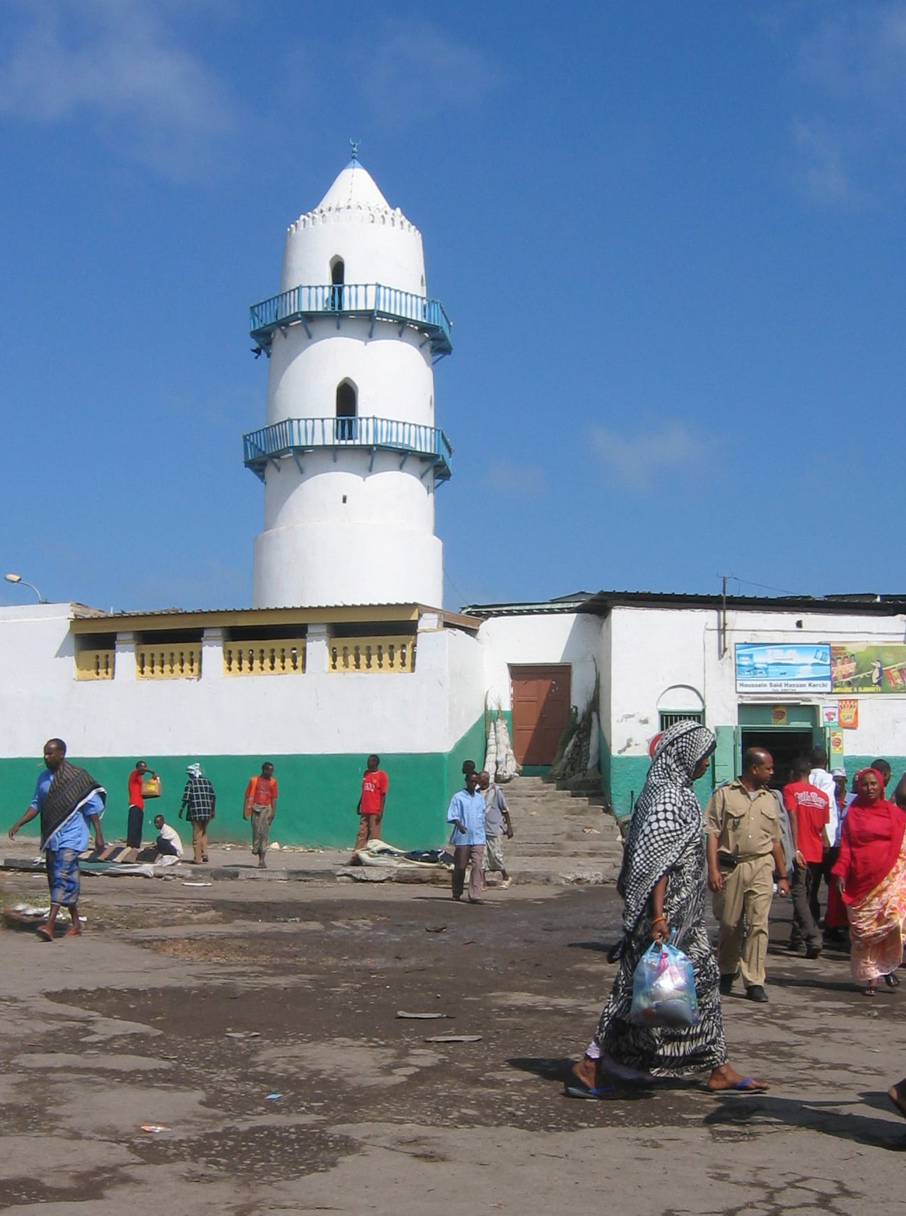 A white mosque with a tall square minaret on a busy city street