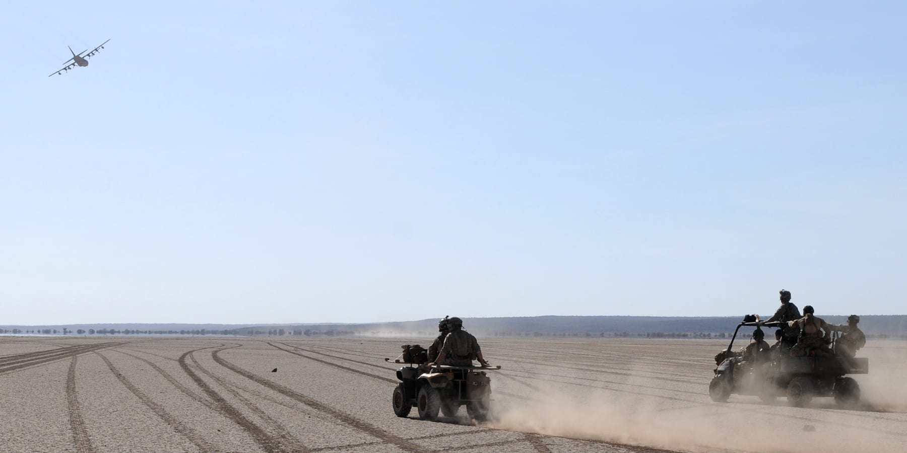 A vast flat pale desert plain stretching to distant hills under a hazy sky