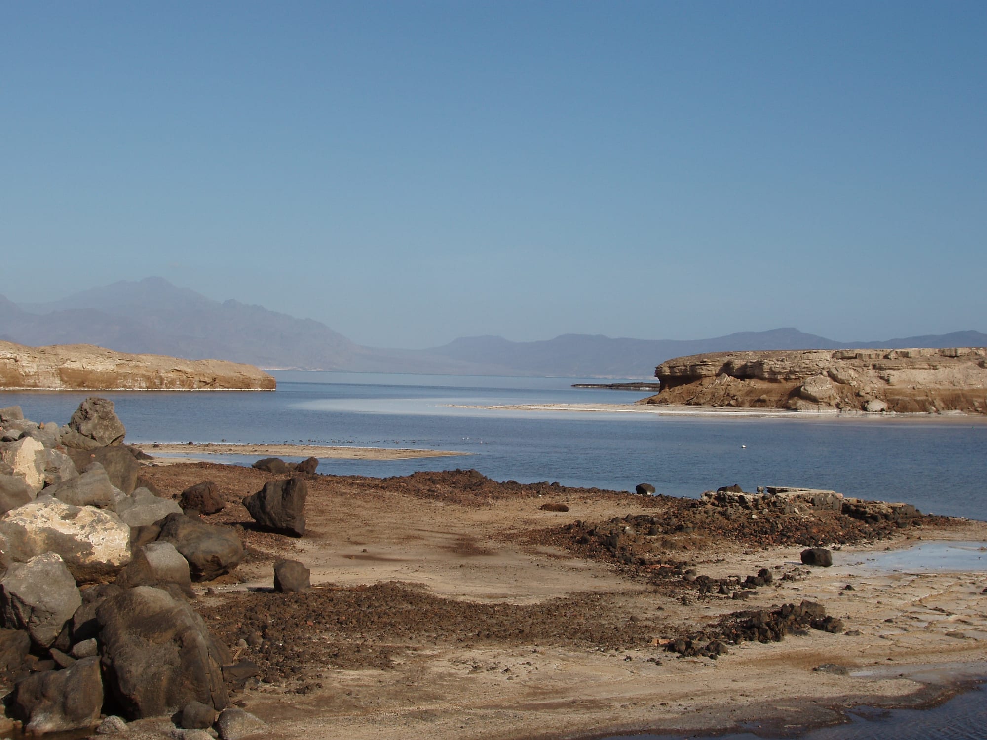 A brilliant white salt shore around a deep blue lake ringed by dark volcanic hills