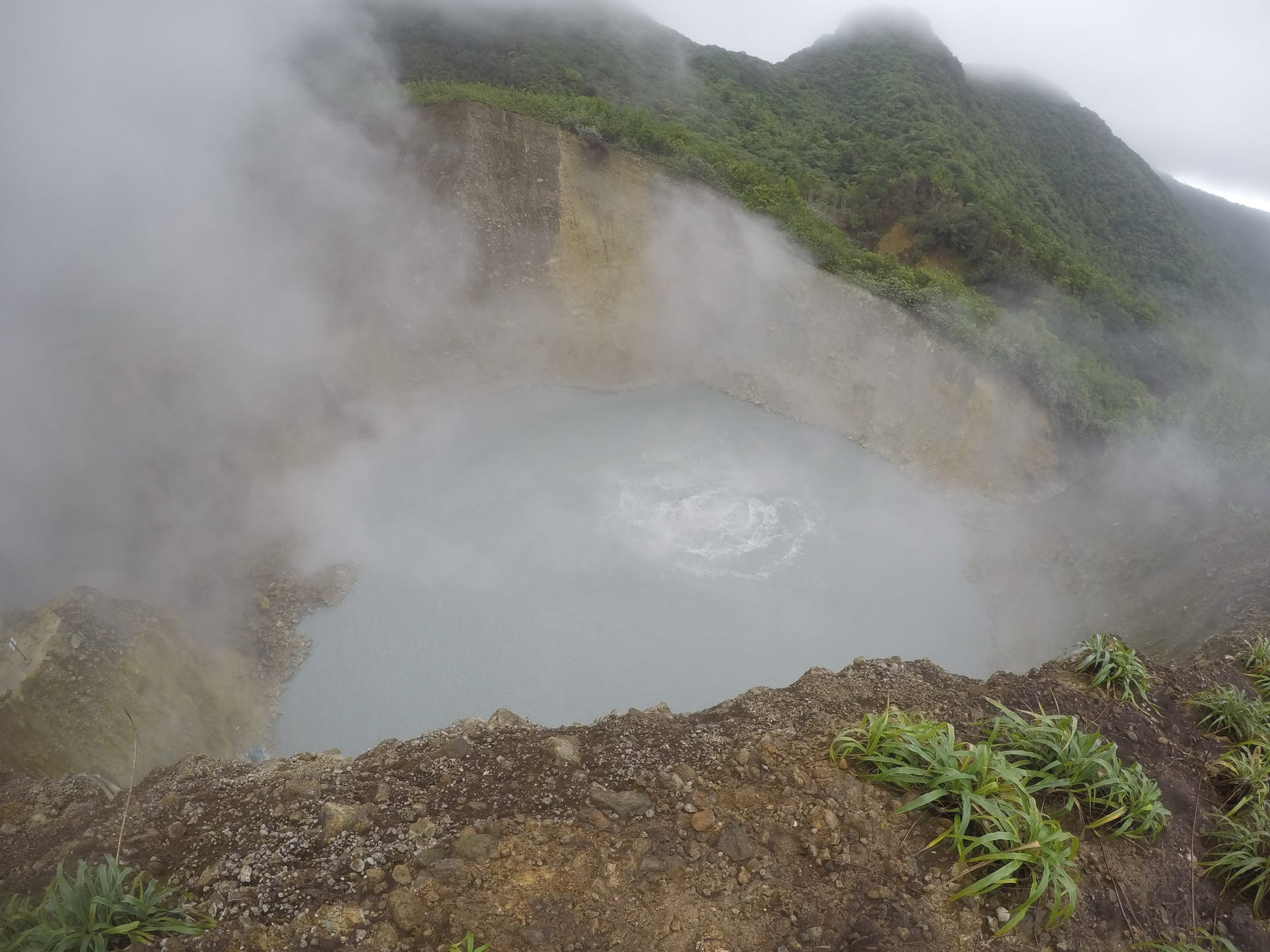A steaming grey-blue lake bubbling at its centre, ringed by steep cliffs
