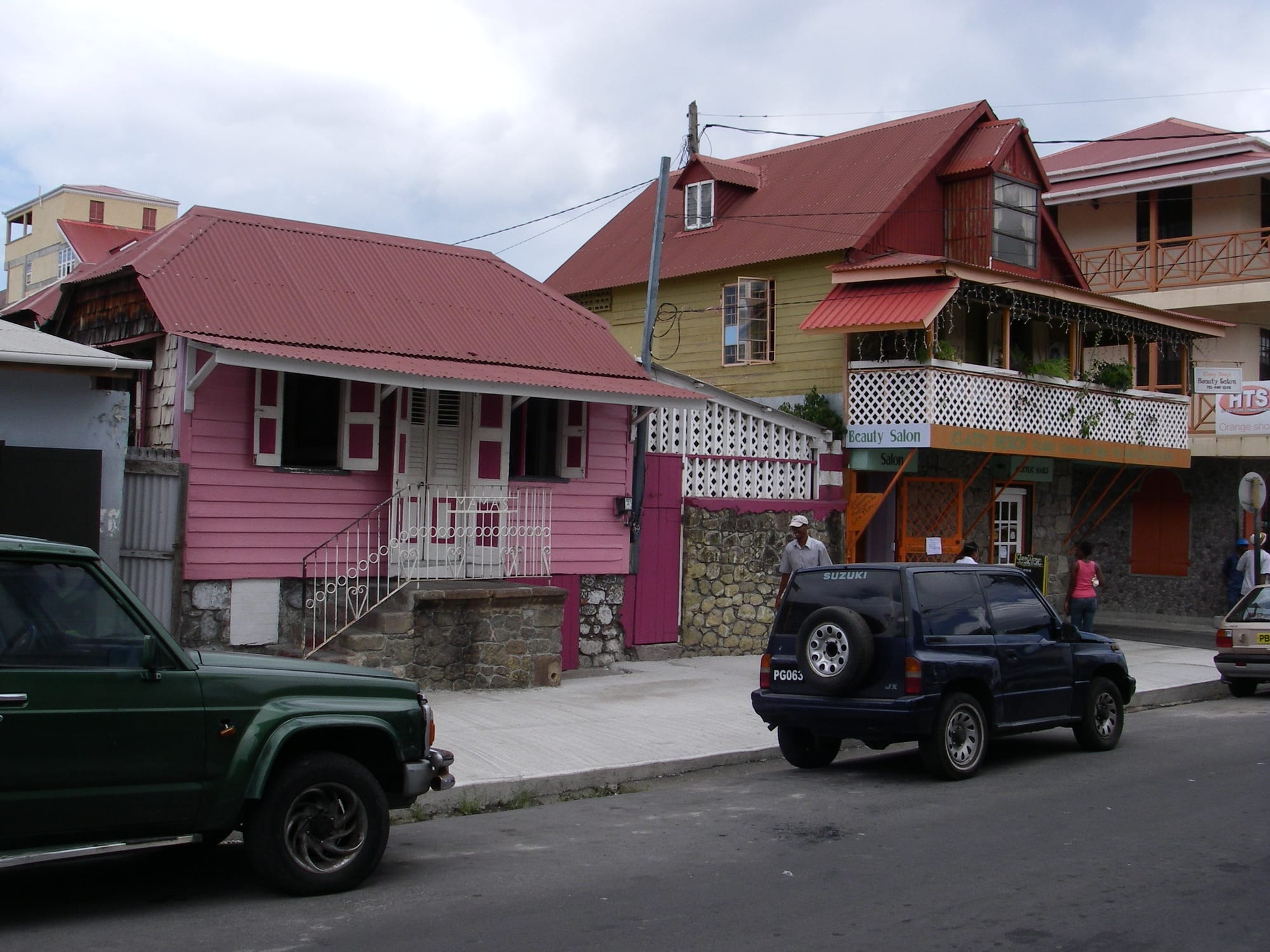 Colourful wooden houses with corrugated metal roofs on a street in Roseau, Dominica, with cars and pedestrians