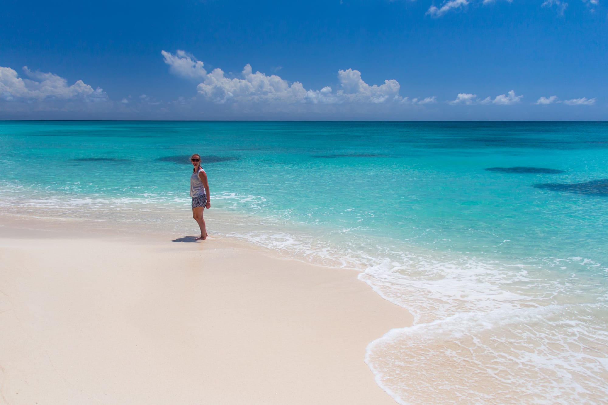 A palm-lined white beach with a wooden boat and clear shallow water