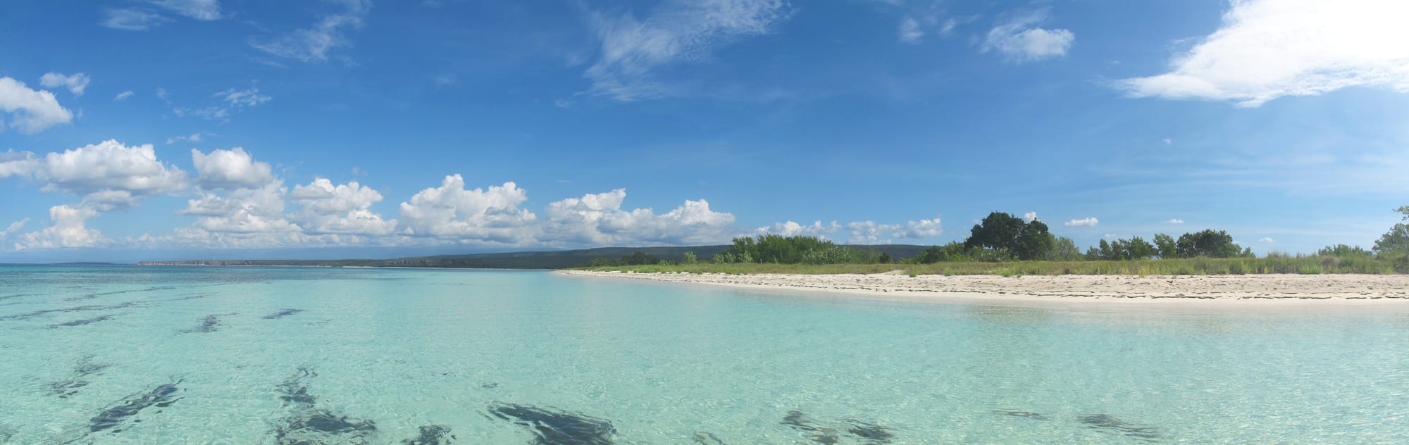 A long empty curve of pale sand and clear turquoise water below arid cliffs, no buildings