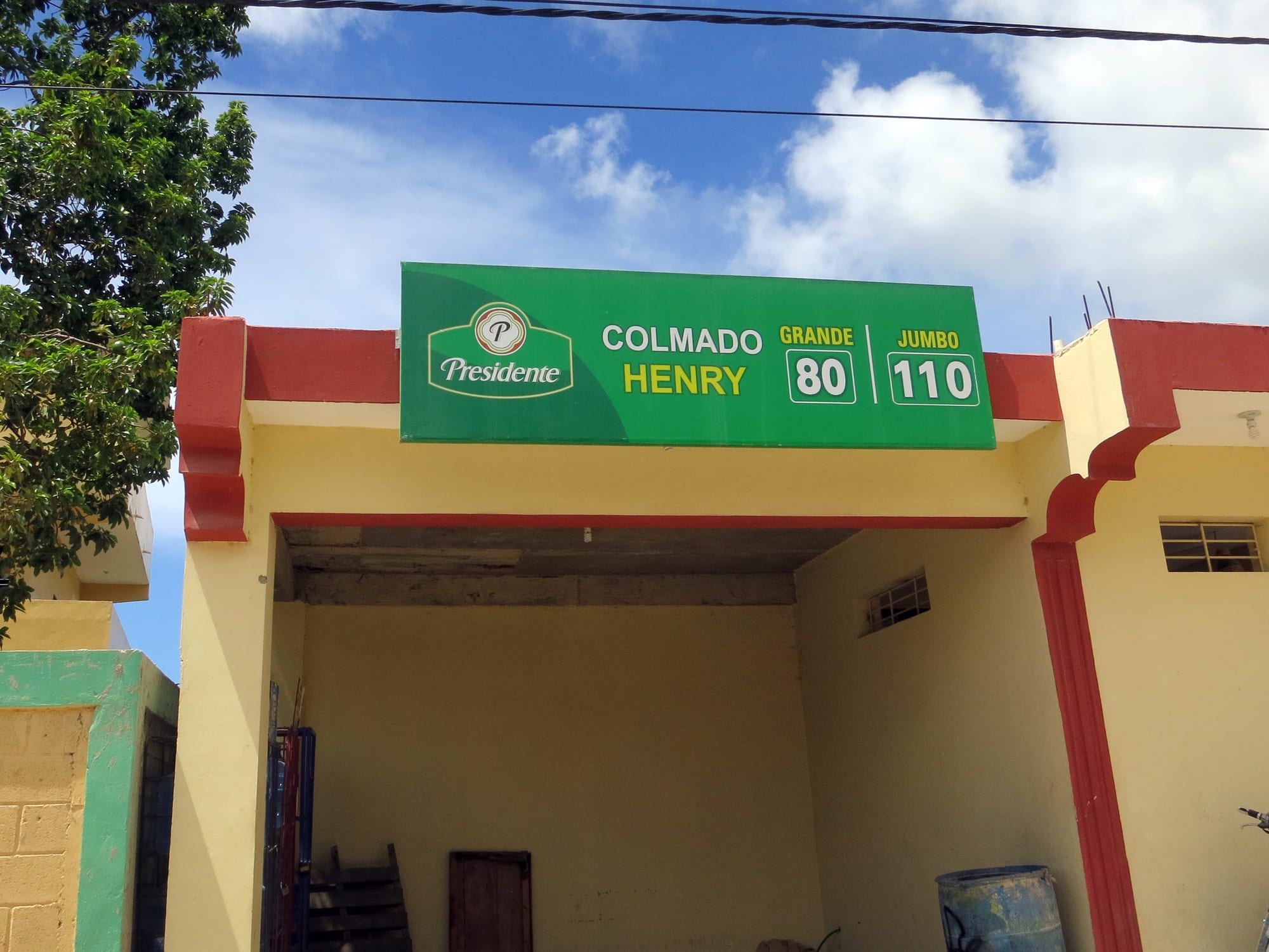 The storefront of a small neighbourhood shop called Colmado Henry, with a green sign advertising Presidente beer