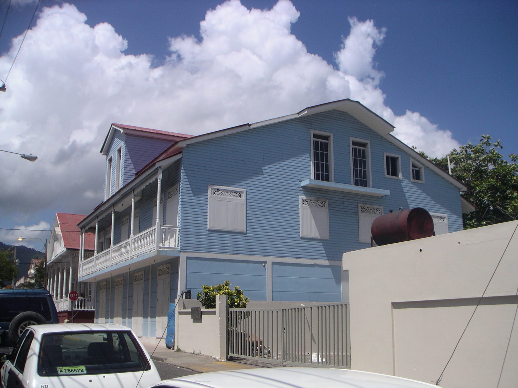 A two-storey wooden house painted pale blue with white gingerbread trim and balconies, on an ordinary residential street