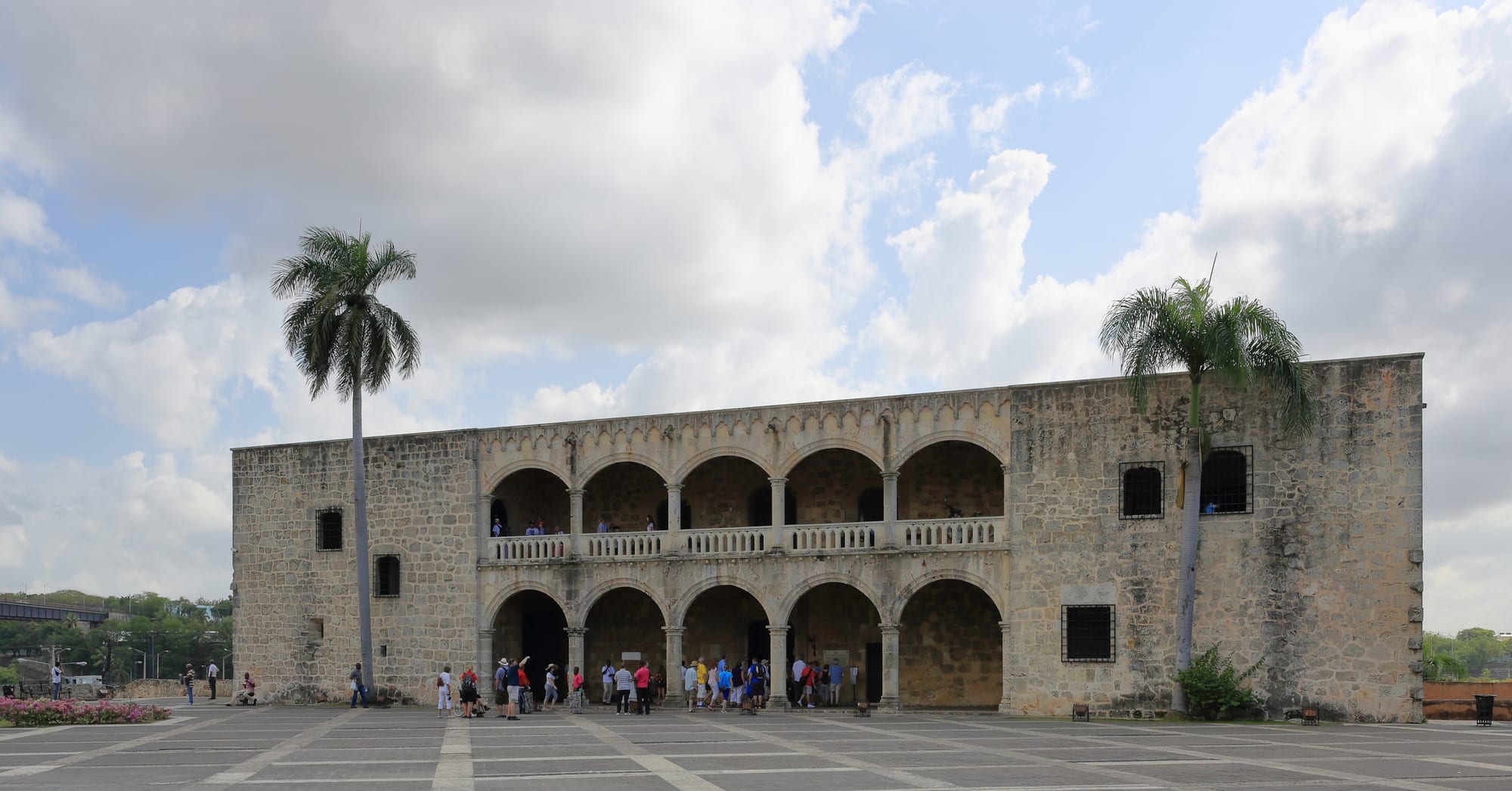 A stern two-storey Renaissance stone palace with double-tiered arcaded loggias, on a plaza