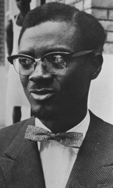A 1960 portrait of Patrice Lumumba in glasses and a goatee, wearing a suit