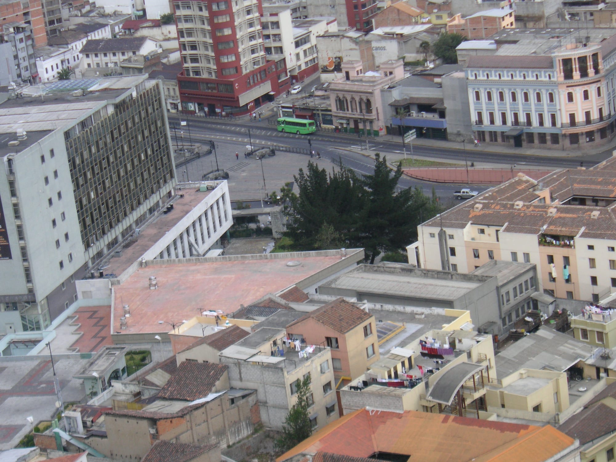 An aerial view over Quito's densely packed rooftops, with laundry hanging out to dry and a bus on a road below