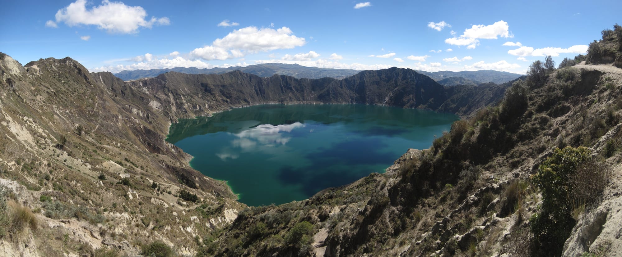 A wide crater holding a still green lake, the rim cliffs dropping steeply to the water