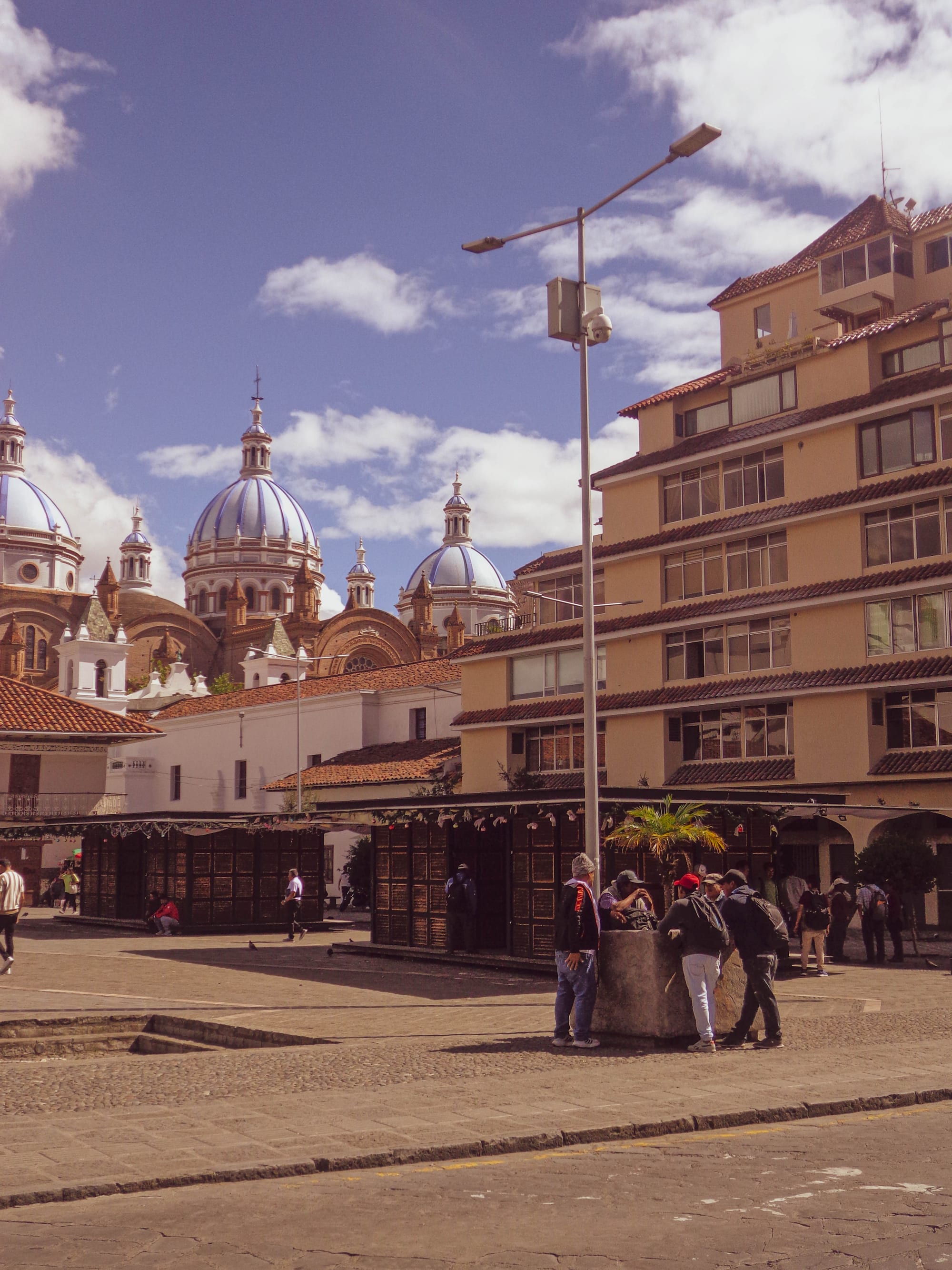 A colonial plaza with a domed church, arcaded buildings, and people gathered