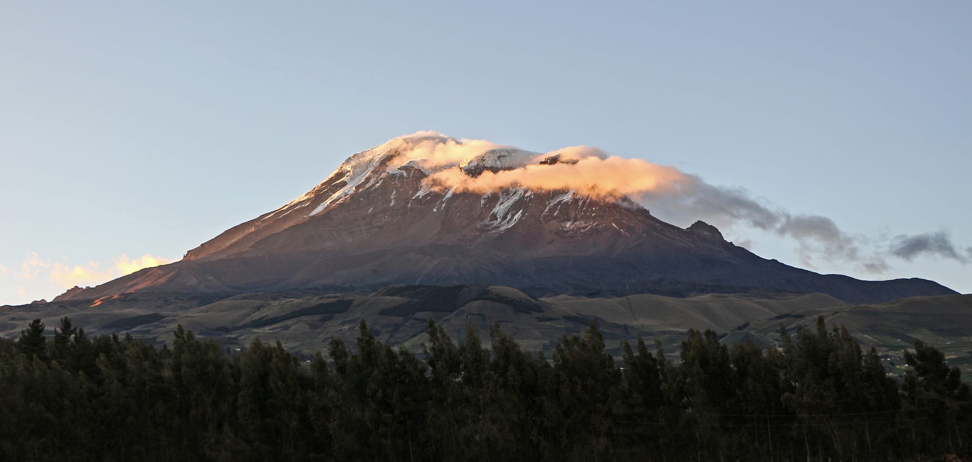 A massive glaciated volcano rising above brown high-altitude plains