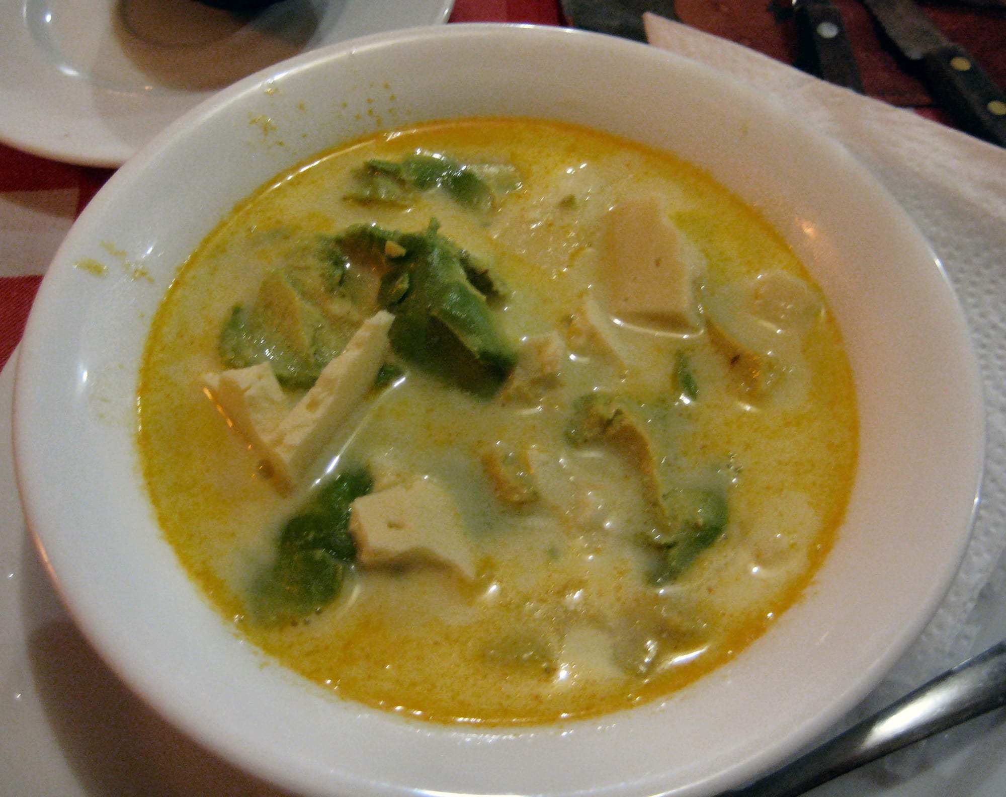 A bowl of thick, pale yellow soup topped with avocado and cheese