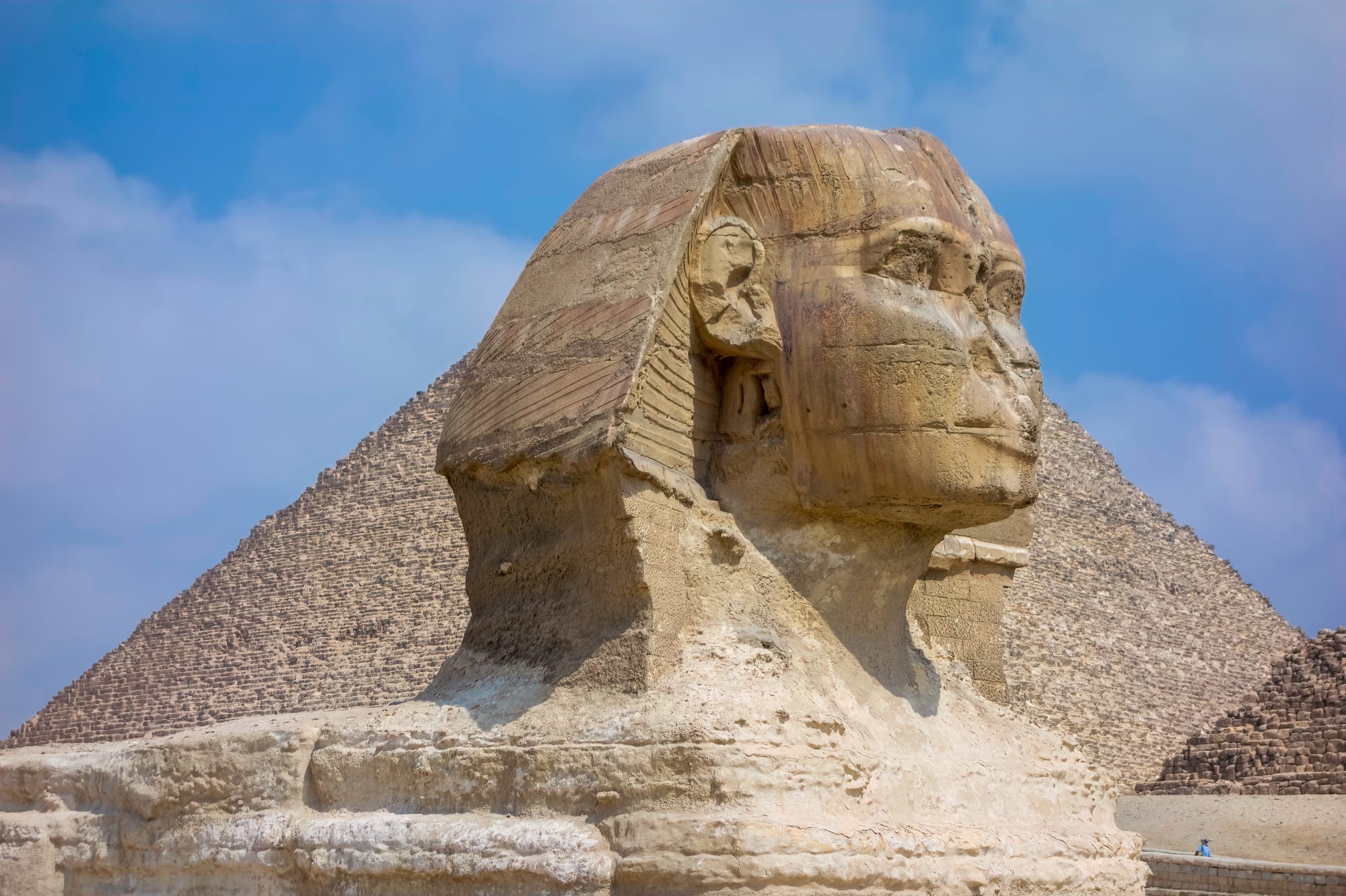 The Great Sphinx with a pyramid rising directly behind it against a clear sky