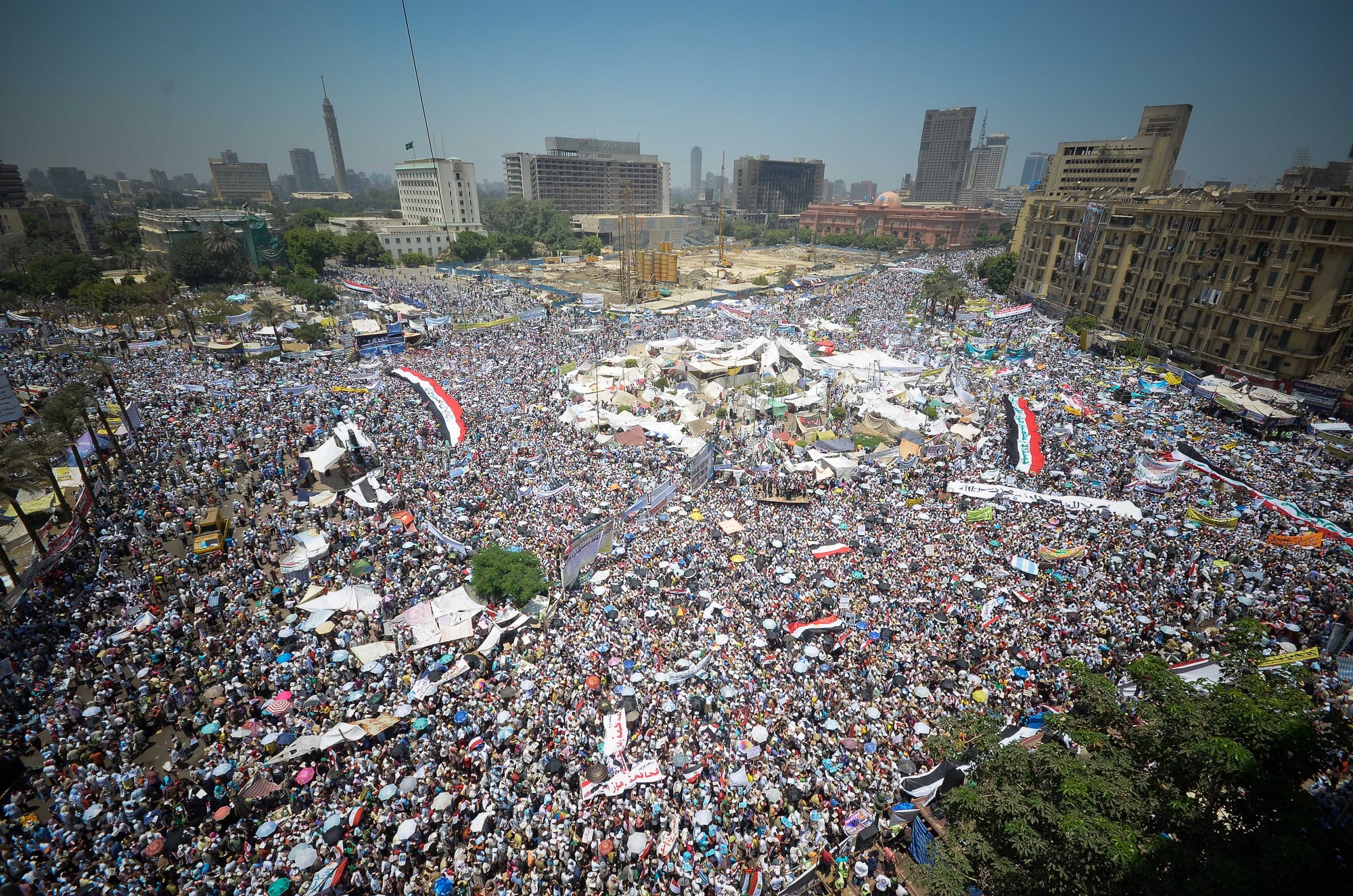 A vast crowd filling a circular city square, with banners and tents, seen from above