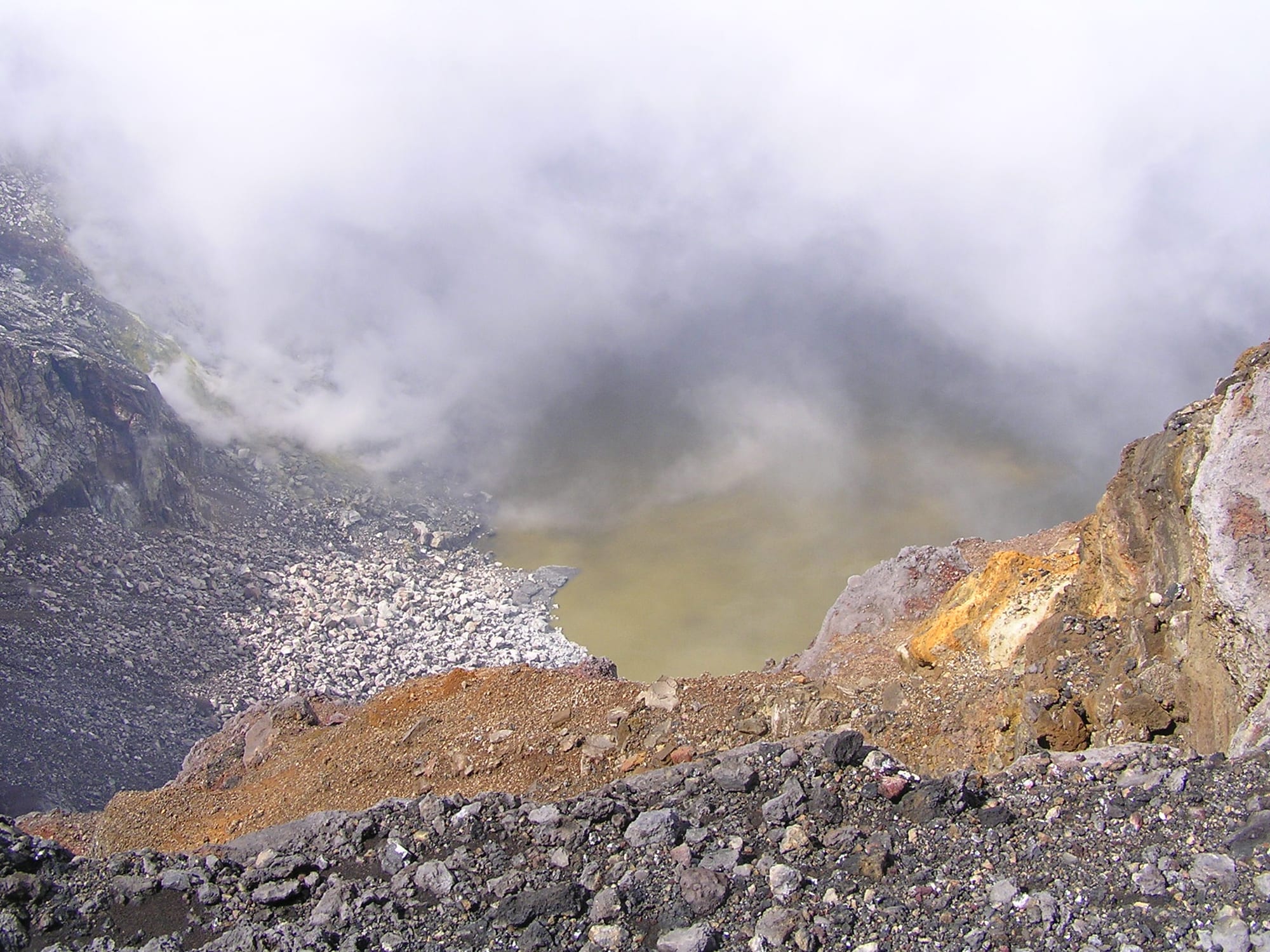 A broad forested volcanic cone rising above farmland and cloud