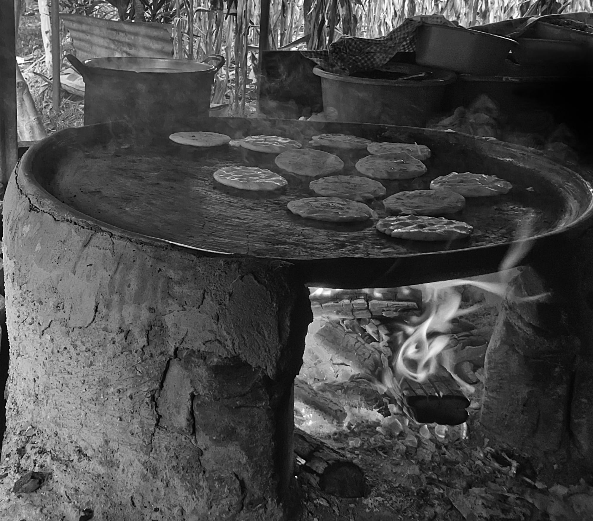 Stuffed corn tortillas cooking on a traditional clay griddle over a wood fire