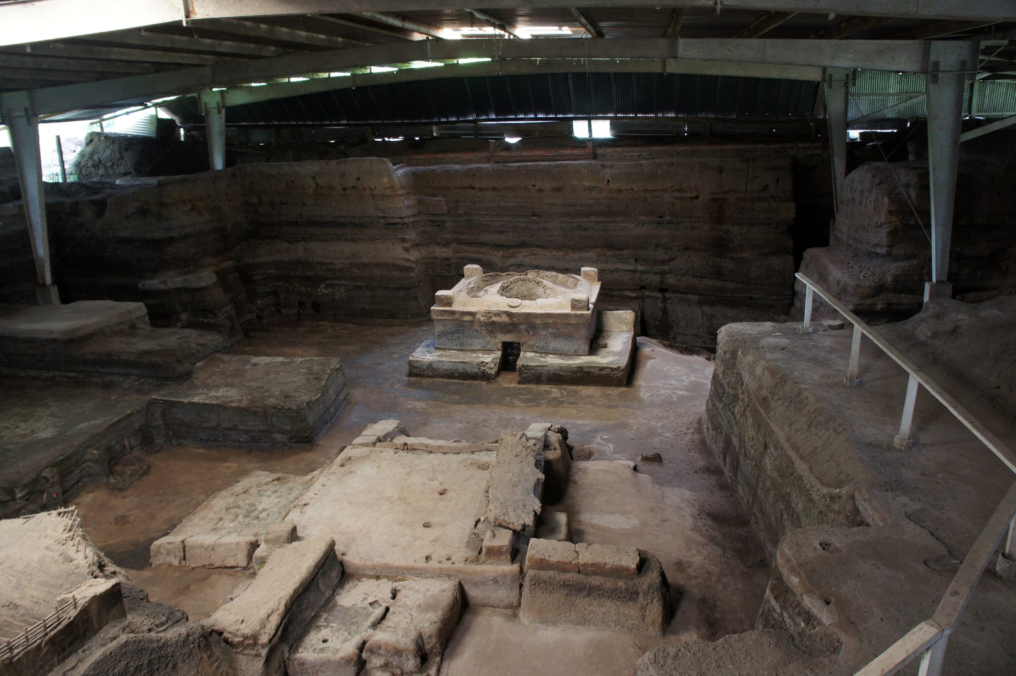 Low adobe walls of an ancient buried house sheltered under a modern metal roof at an excavation