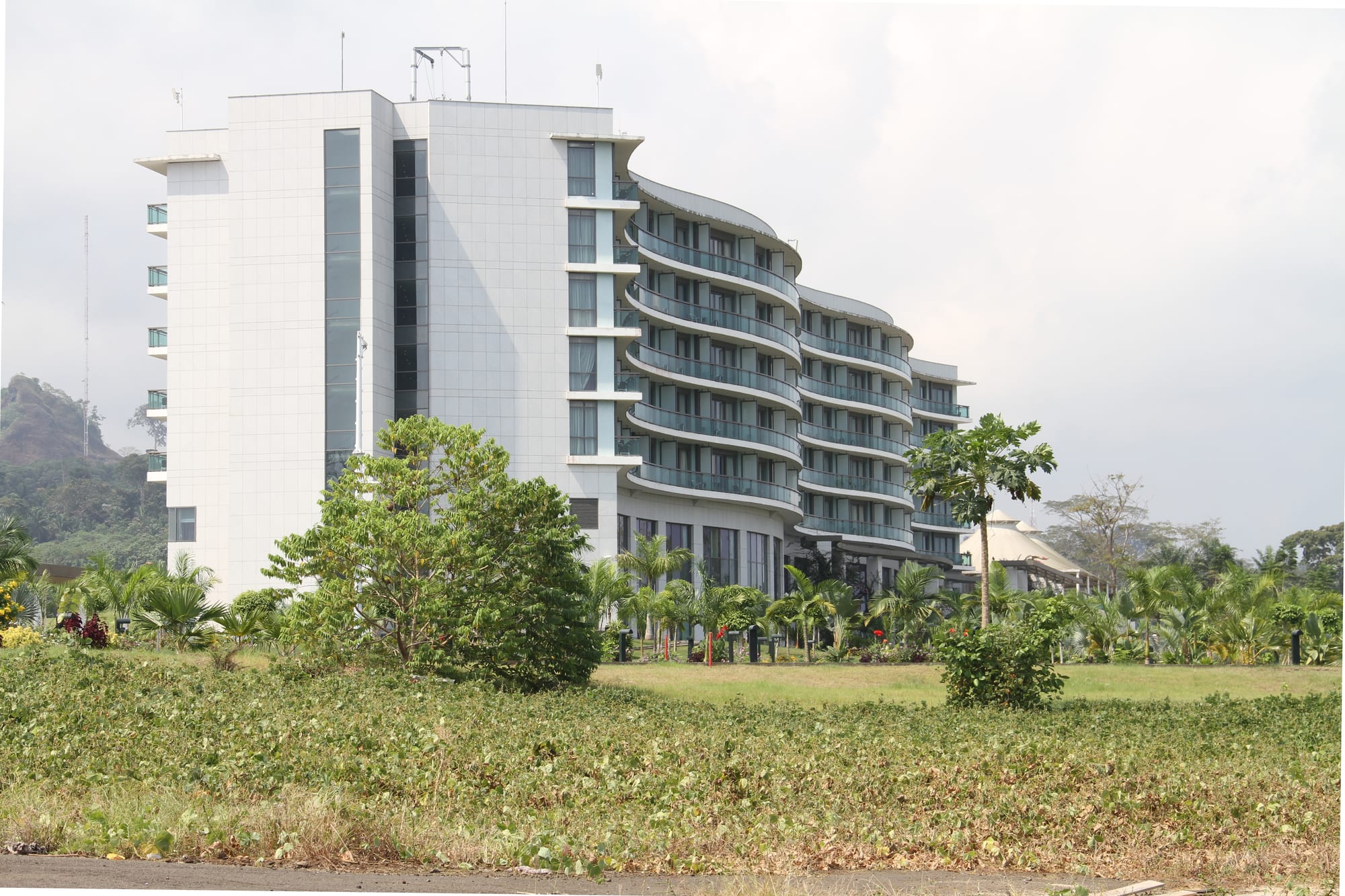 A curving modern luxury hotel building surrounded by manicured tropical gardens