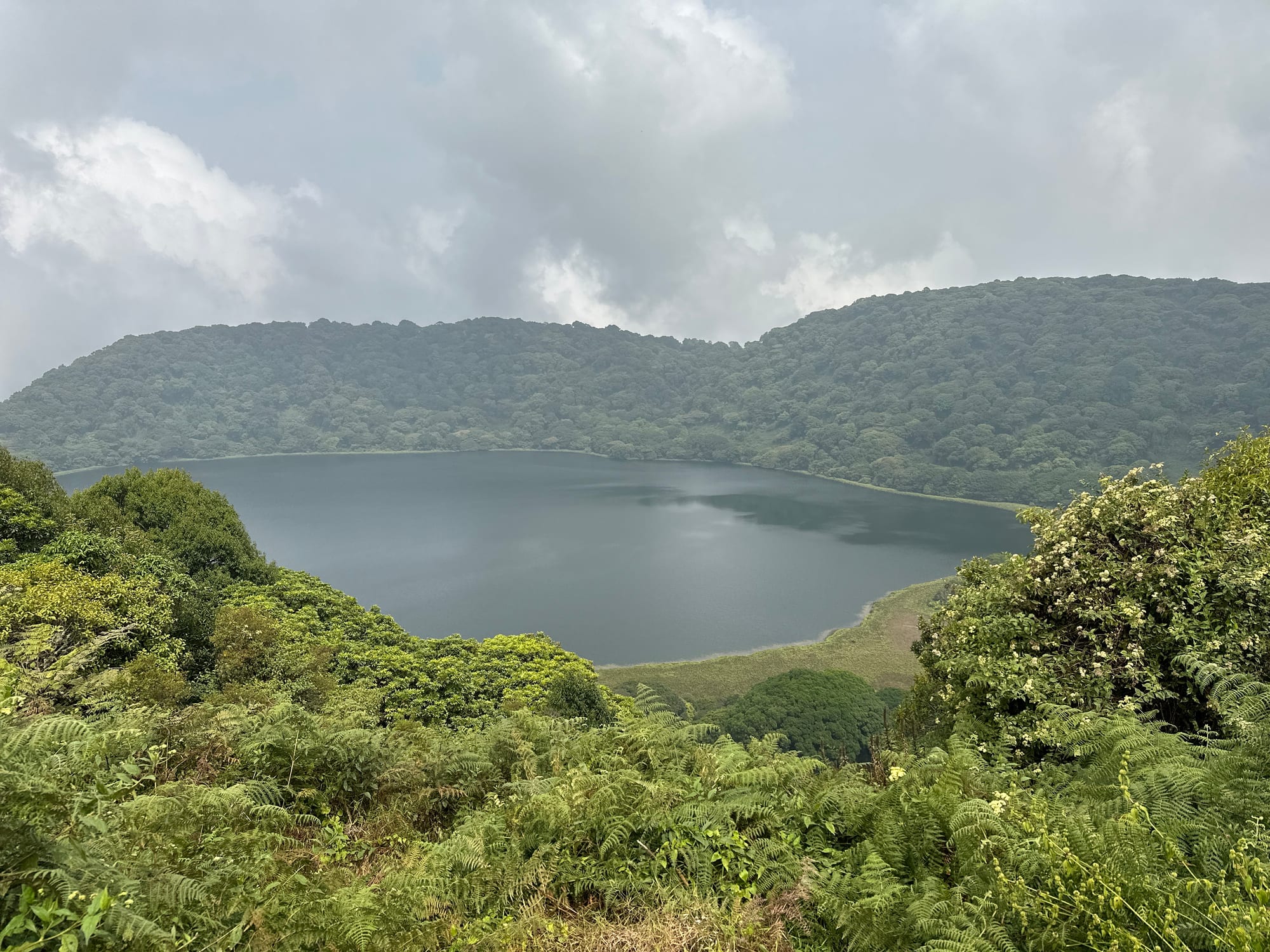 A still, dark crater lake enclosed by steep, densely forested slopes