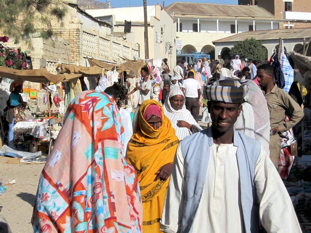 A busy street market crowd in Keren, with women in brightly patterned shawls and stalls of goods along both sides