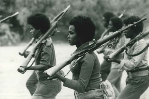 Women in fatigues carrying rifles, seated together during the independence war
