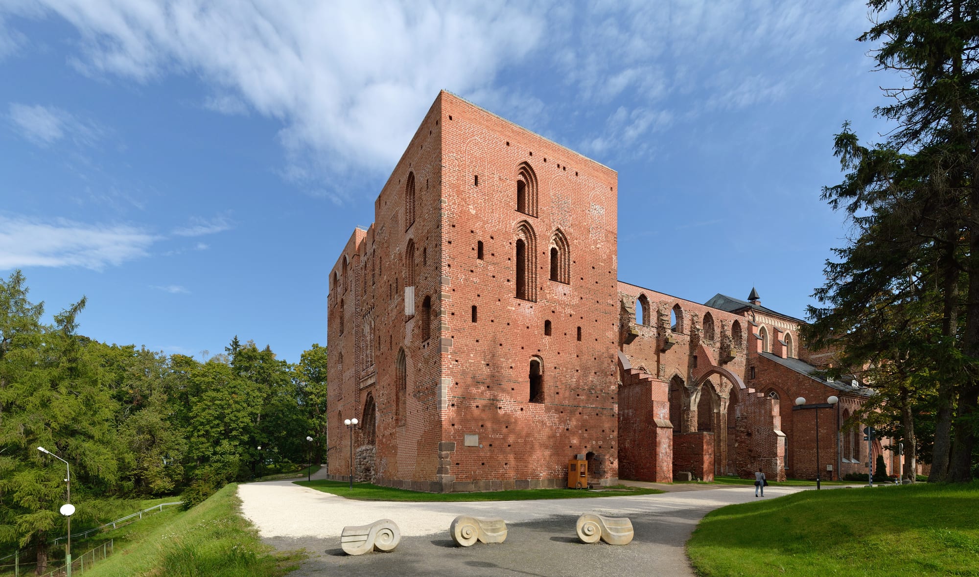 The tall red-brick ruined nave of a Gothic cathedral on a wooded hill