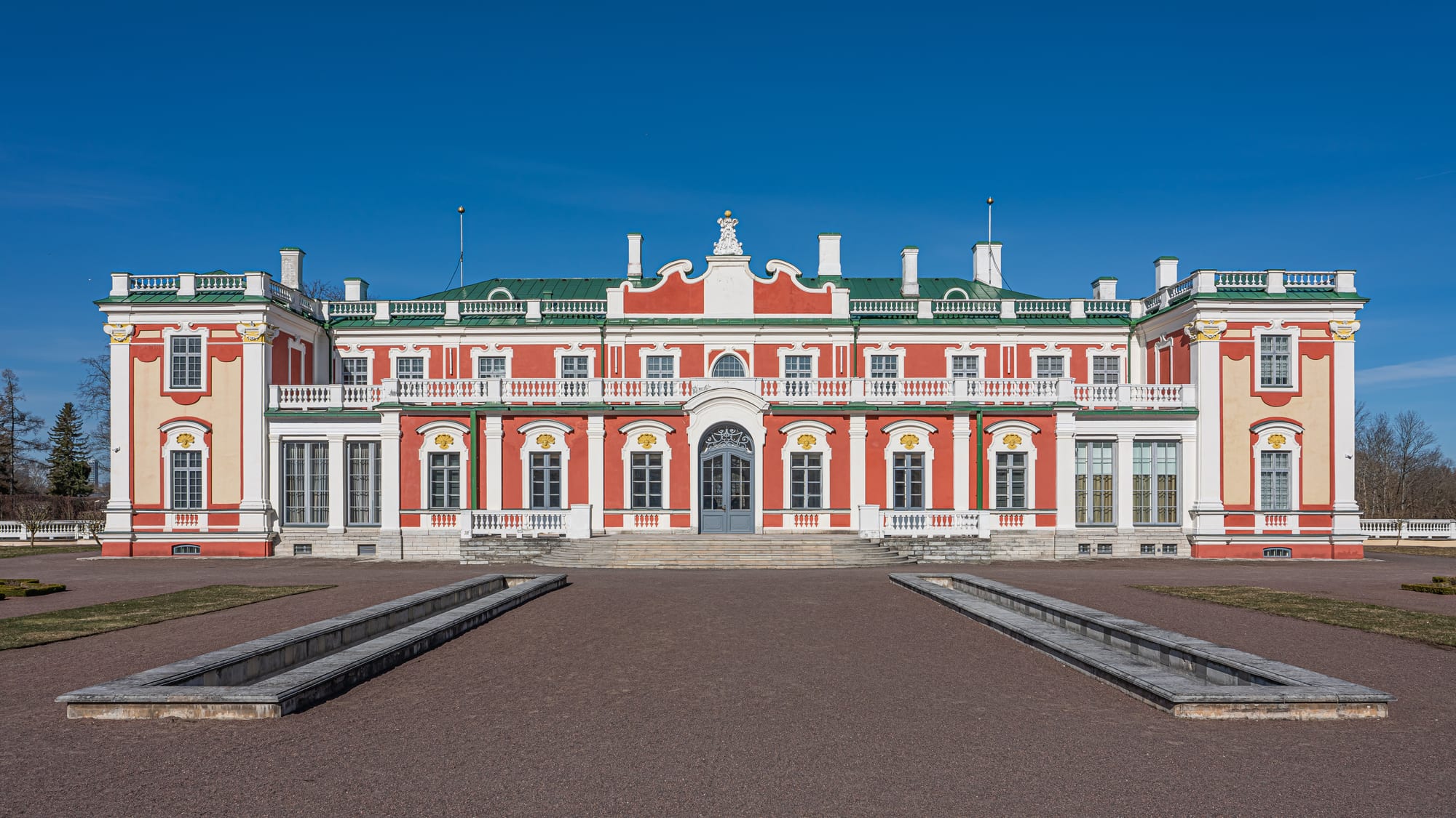 A pink-and-white Baroque palace behind a formal parterre garden with a fountain
