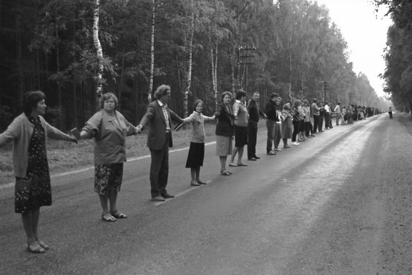 A long line of people holding hands along a rural road during the Baltic Way