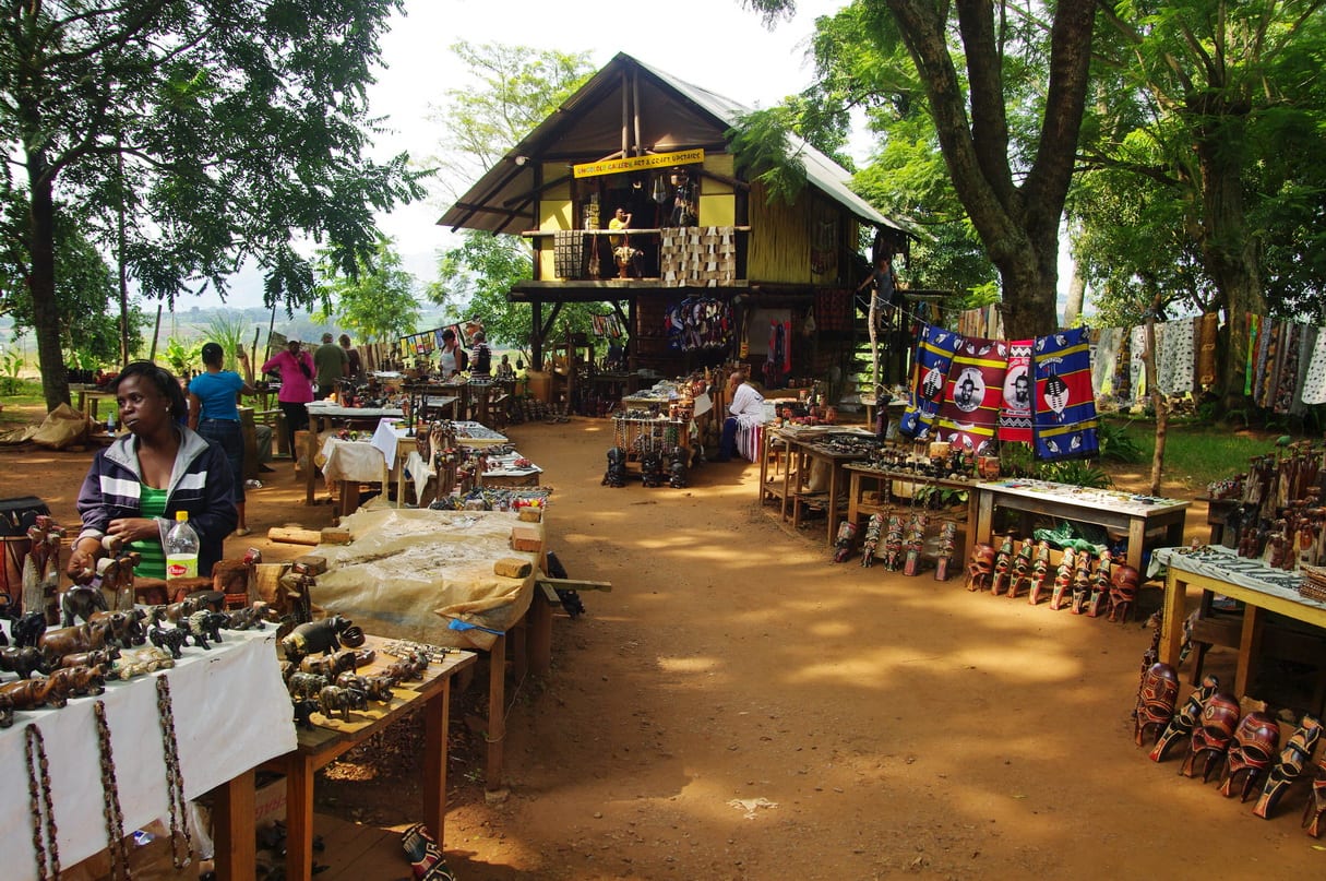 An open-air crafts market at Matsapha in Eswatini, with wooden carvings, beadwork and batik cloth laid out on tables under trees