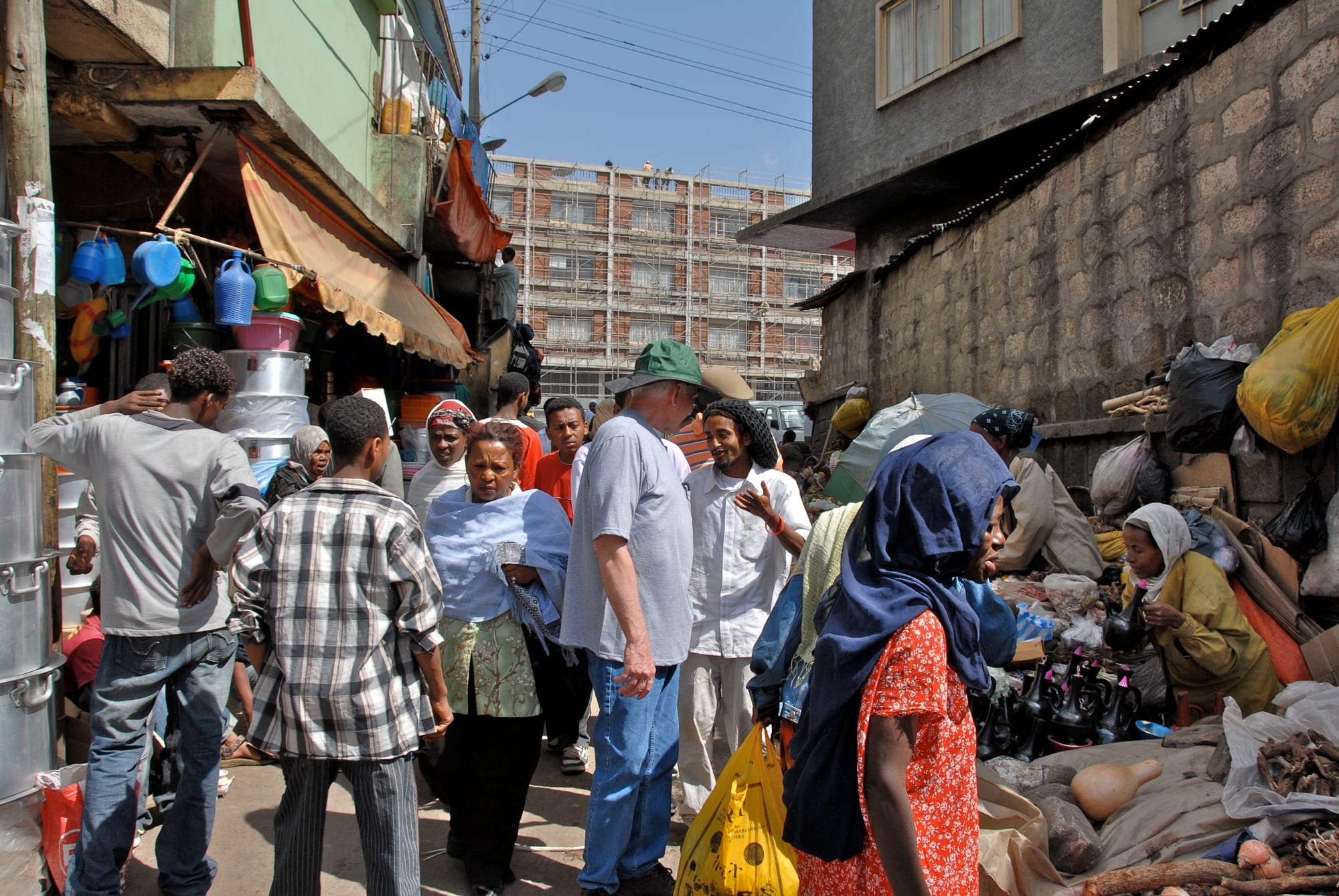A crowded narrow lane in Addis Ababa's Merkato market, with vendors, shoppers, and stalls of household goods