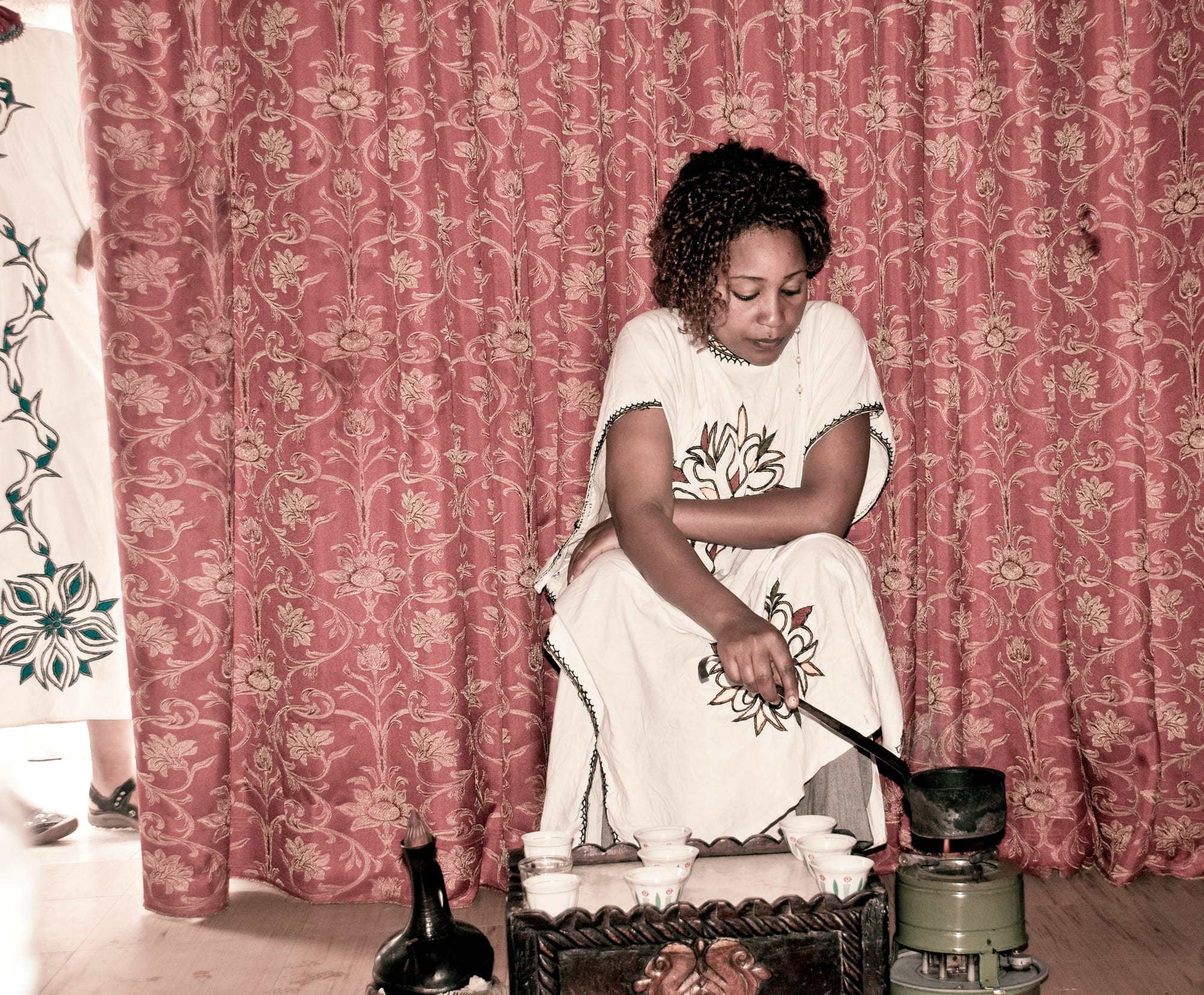 A woman in traditional dress pouring coffee from a black clay pot into small cups