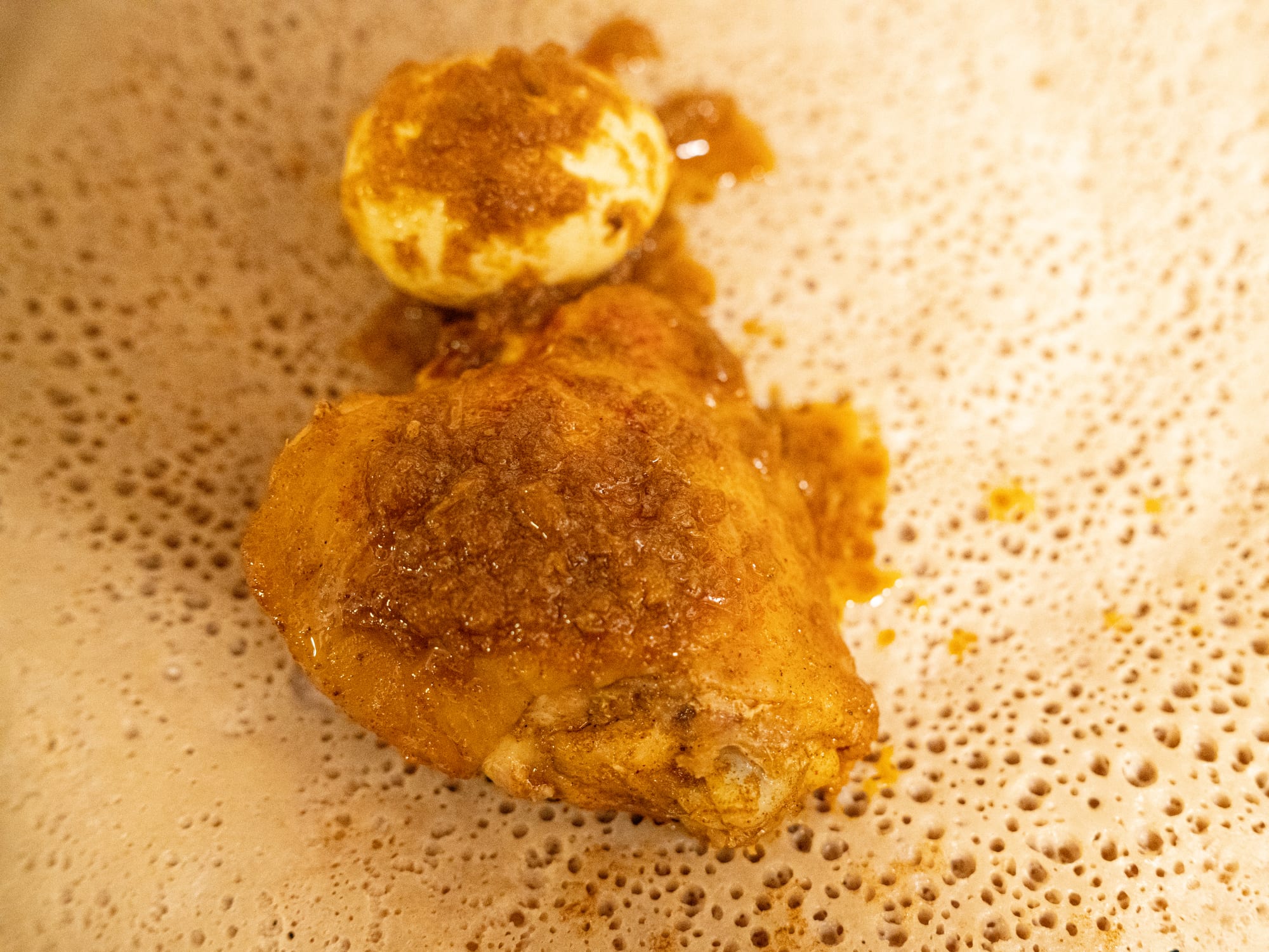 A large round of spongy flatbread topped with a dark red chicken stew and hard-boiled eggs