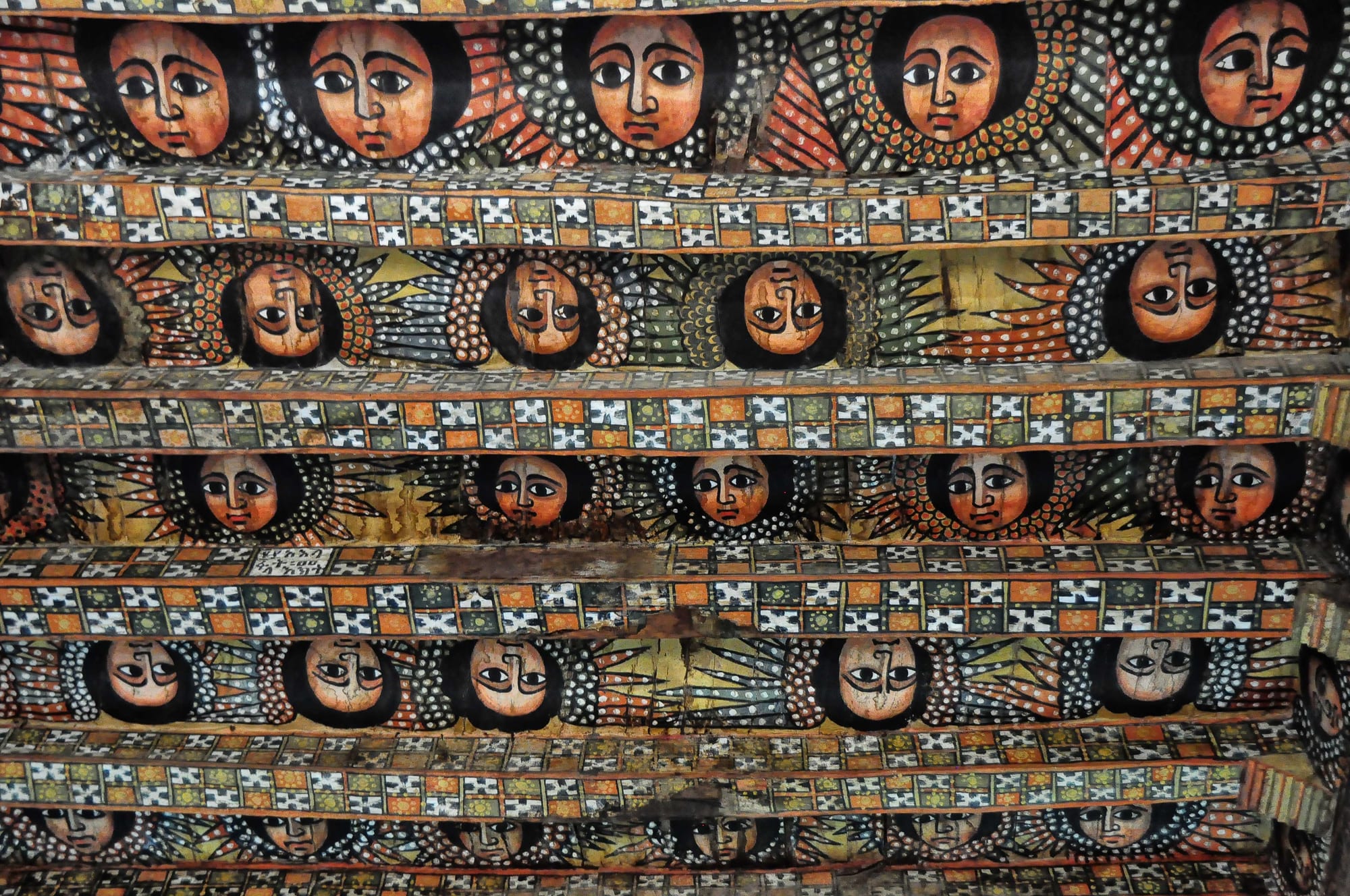 A wooden church ceiling painted with rows of winged angel faces with large dark eyes, separated by beams decorated in a chequered pattern