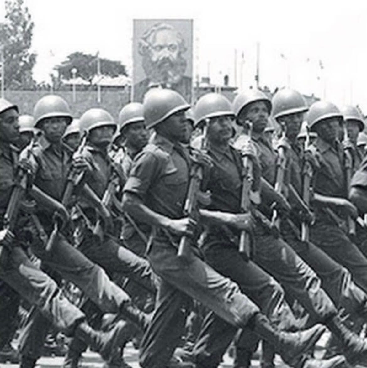 Soldiers and armoured vehicles in a large military parade under red banners