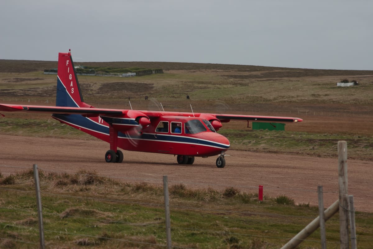 A small red and blue FIGAS Britten-Norman Islander aircraft on a gravel airstrip on Sea Lion Island, Falkland Islands