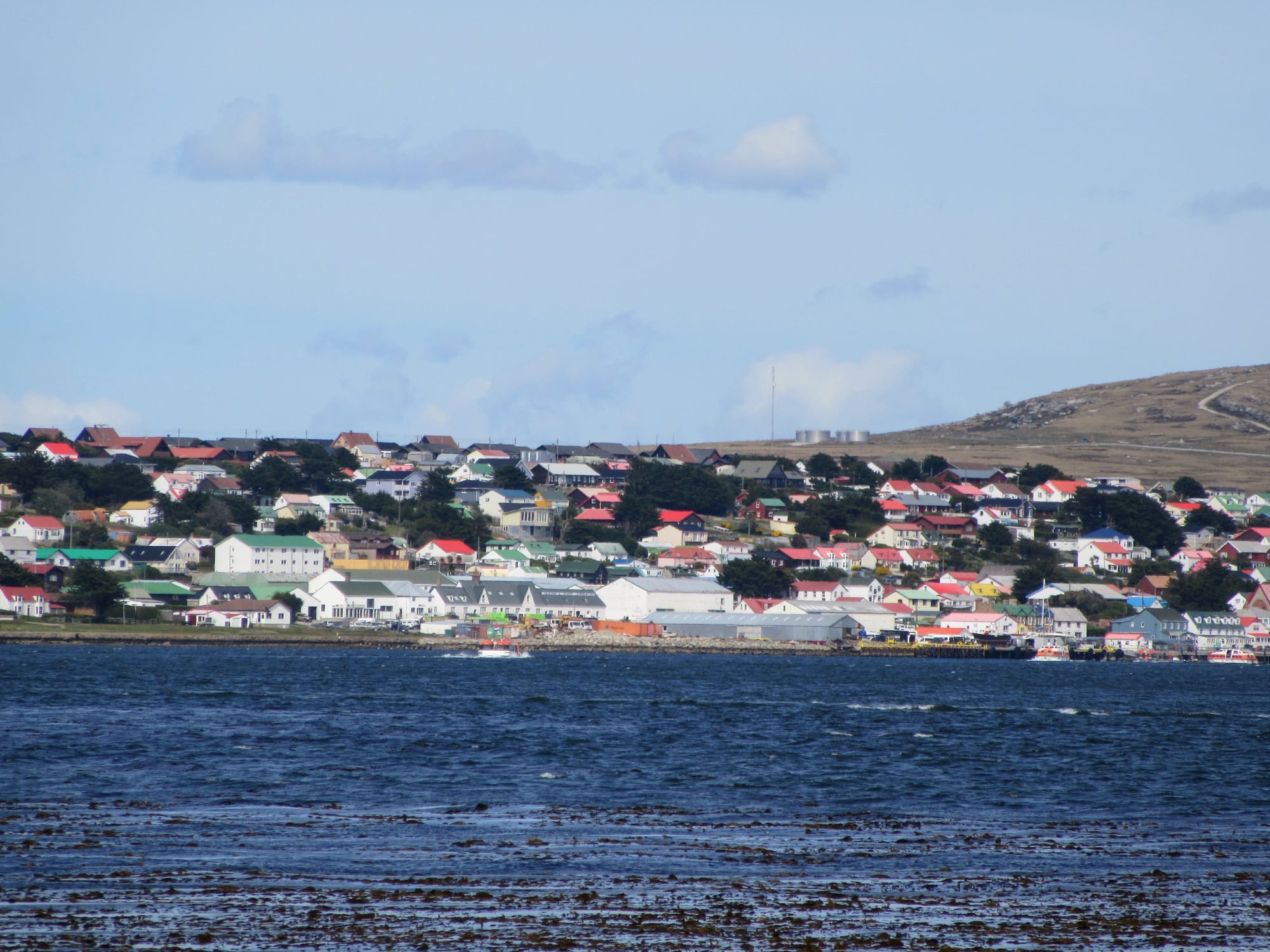A hillside of brightly painted houses with red, green and blue roofs overlooking a harbour in Stanley, Falkland Islands
