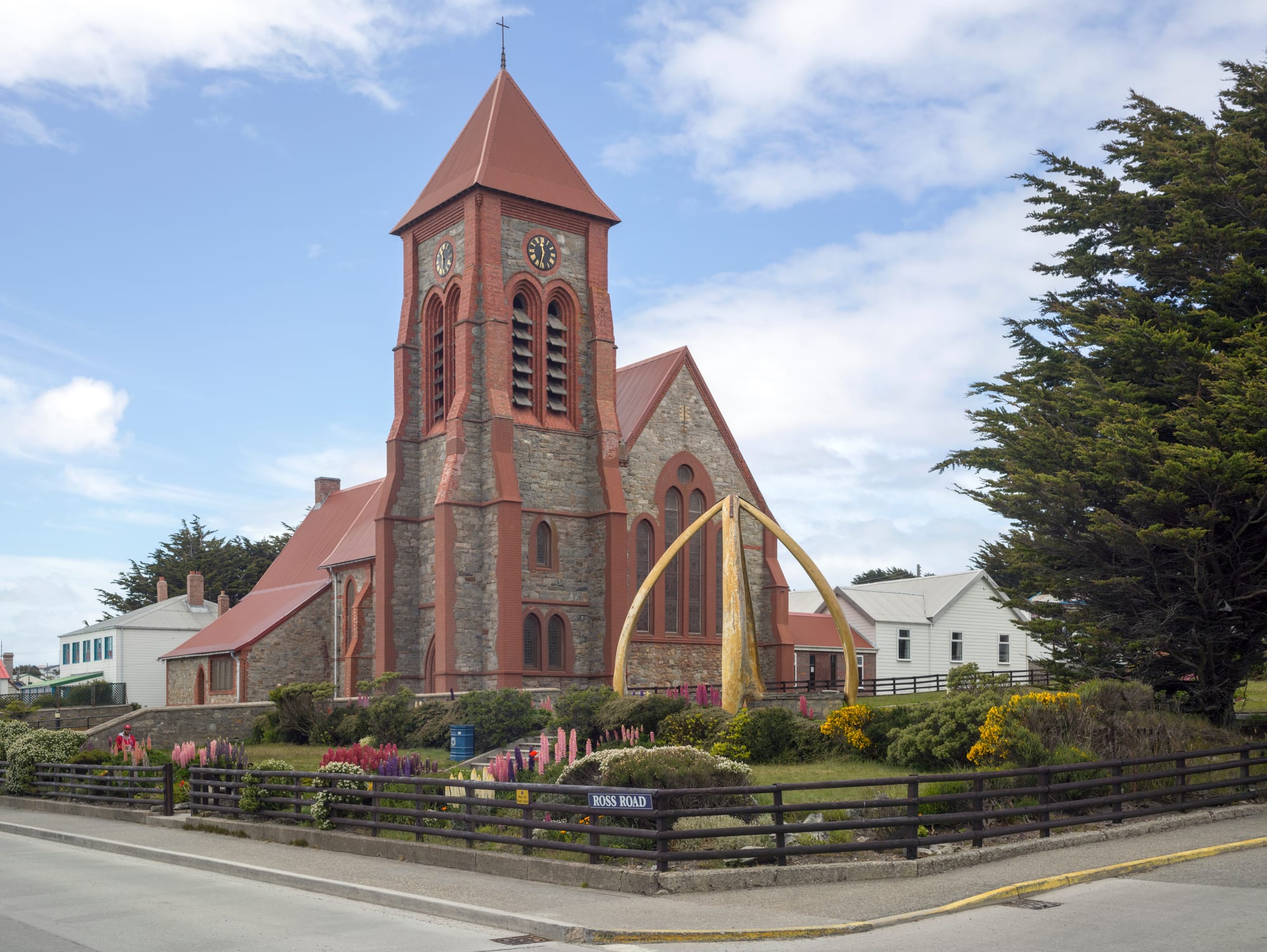 A small stone-and-brick cathedral with a red roof, a whalebone arch on the lawn in front