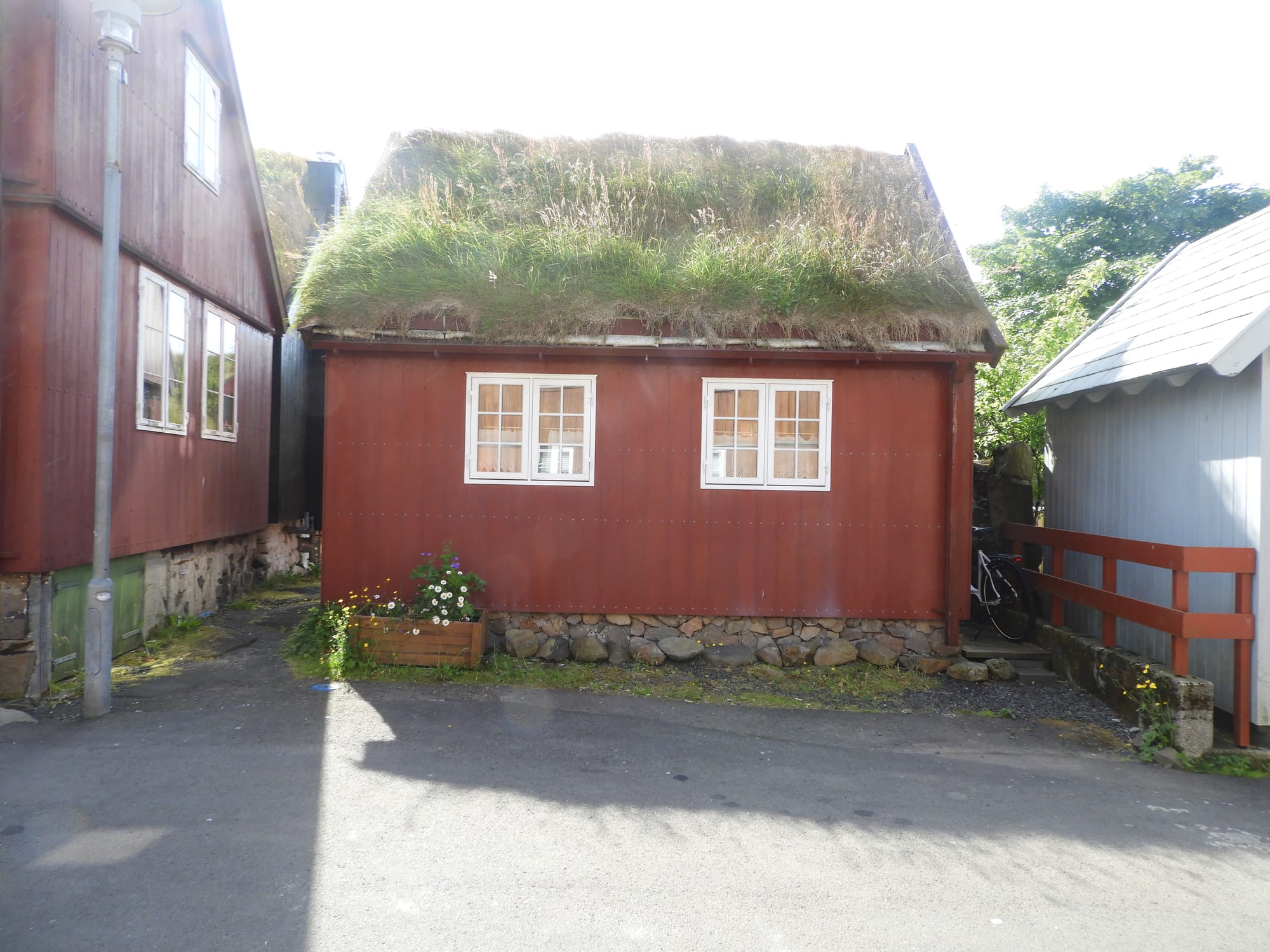 A traditional red wooden house in Tórshavn with a thick, grass-covered turf roof, flowers growing beside the door