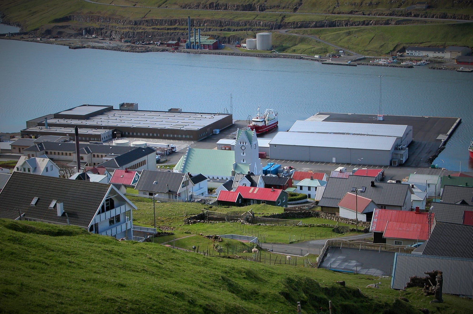 A fishing town on Suðuroy island in the Faroe Islands, with a church, a fish factory, and a docked trawler beside a calm fjord