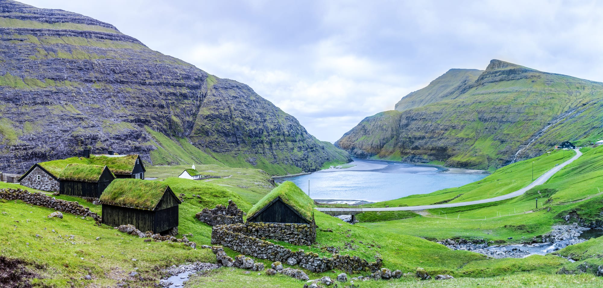 A few turf-roofed houses and a small stone church around a tidal lagoon ringed by steep green mountains