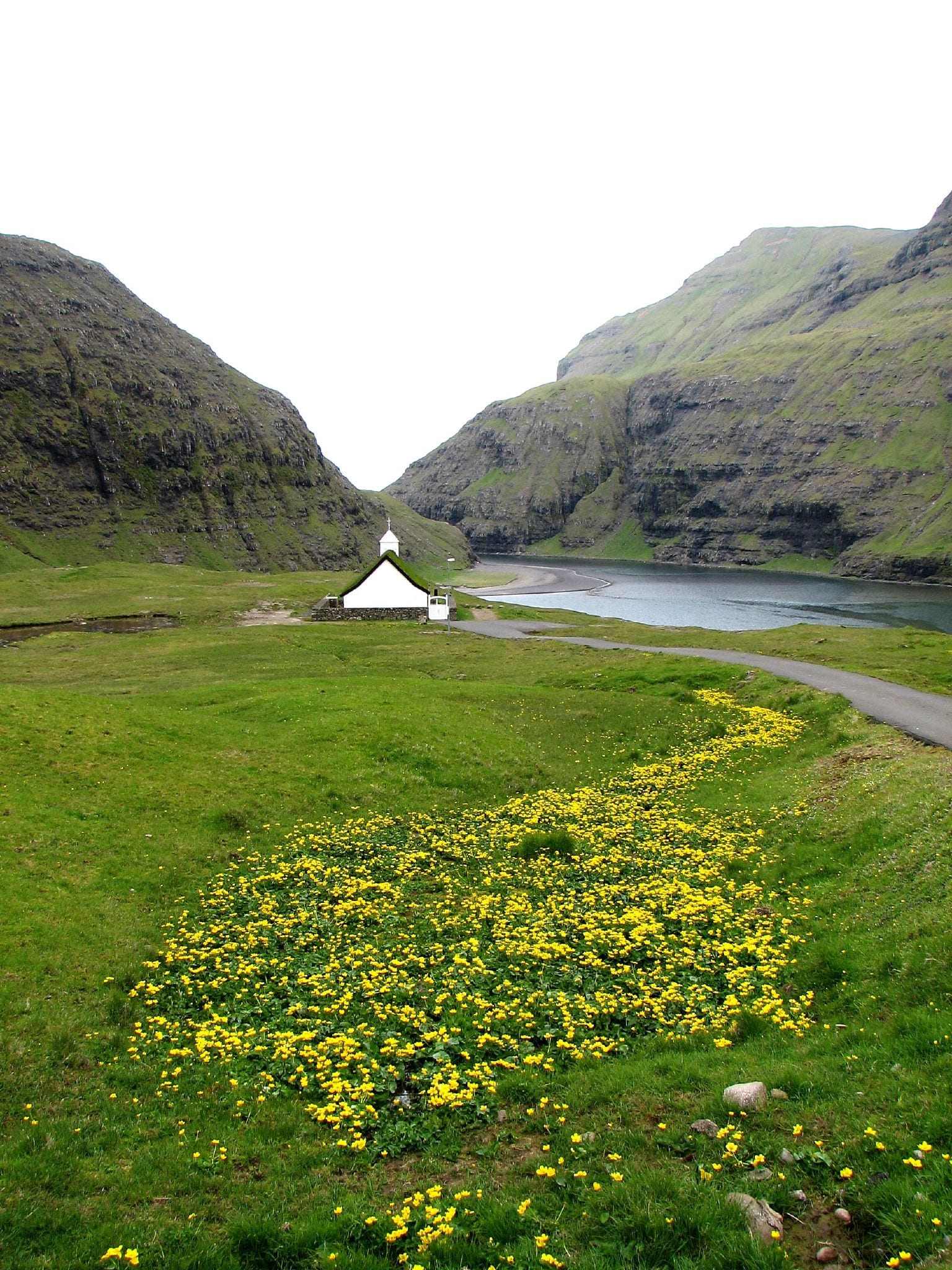 A small white church with a turf roof beside a lagoon under steep mountains
