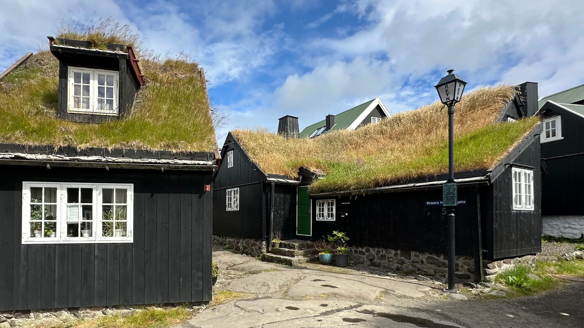 A narrow lane of black timber houses with white window frames and grass roofs