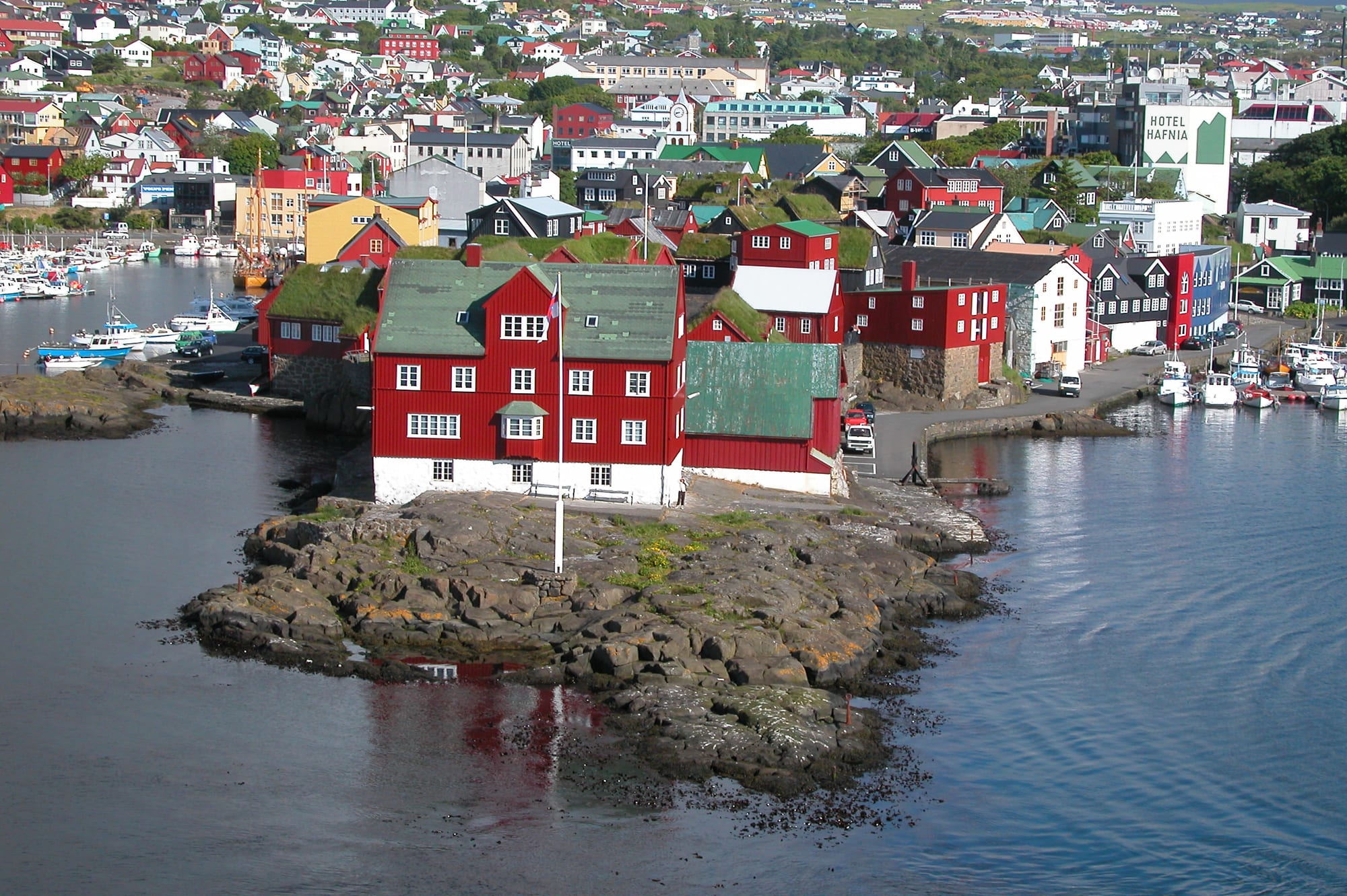 A cluster of small red timber buildings with turf roofs on a rocky harbour peninsula