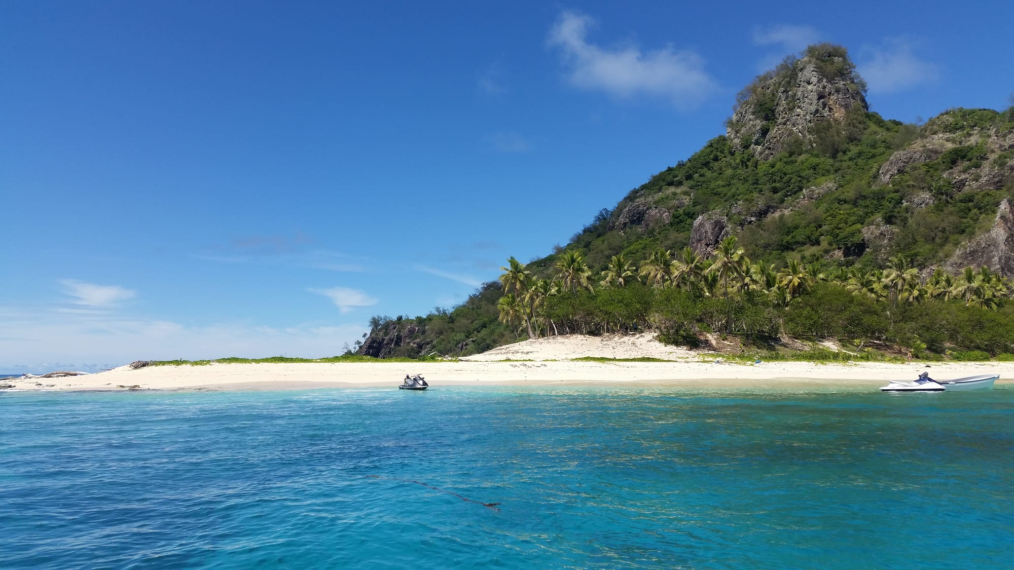 A tiny uninhabited island of white sand and palms ringed by a reef in bright turquoise water
