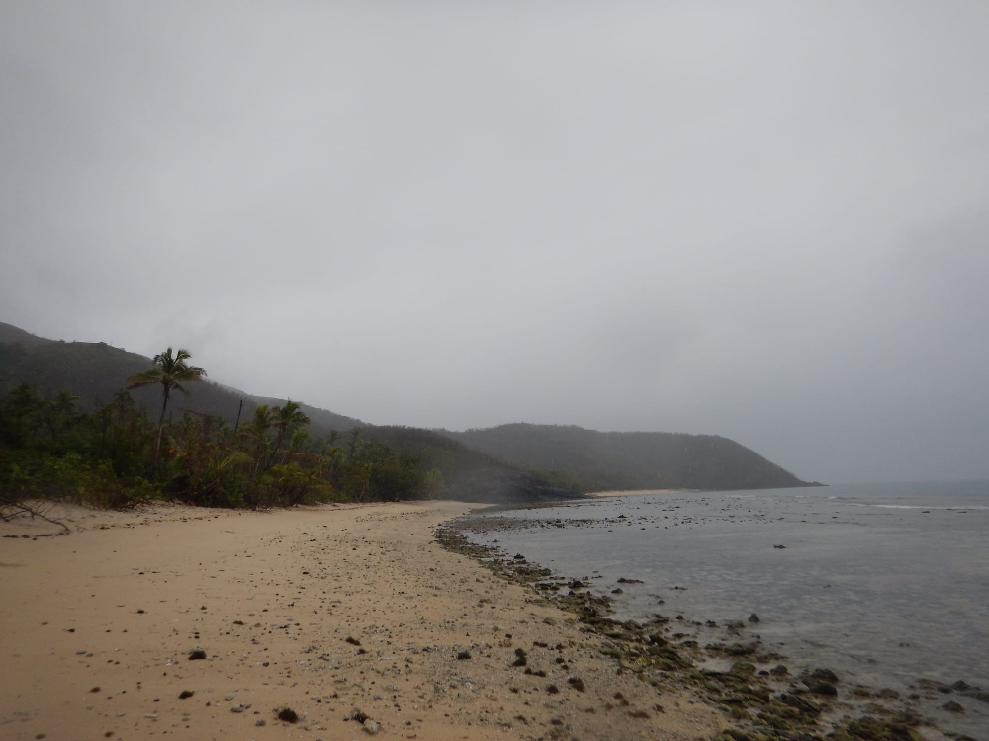 A wide, empty white-sand beach curving along clear shallow water
